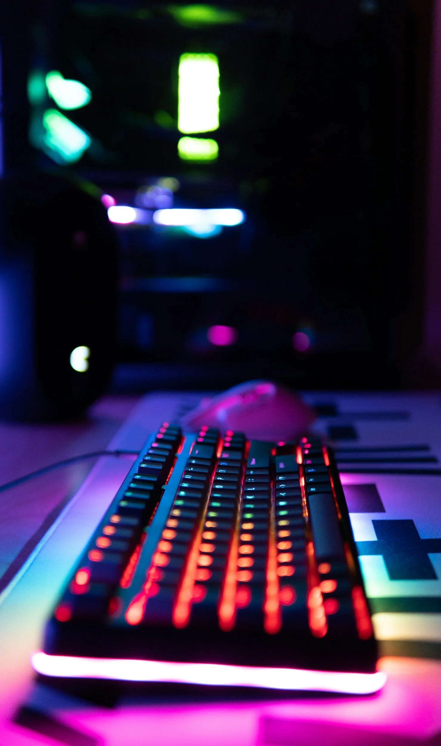Close-up of a computer keyboard with RGB lighting, set in a dark environment with colorful lights reflecting off the surface.