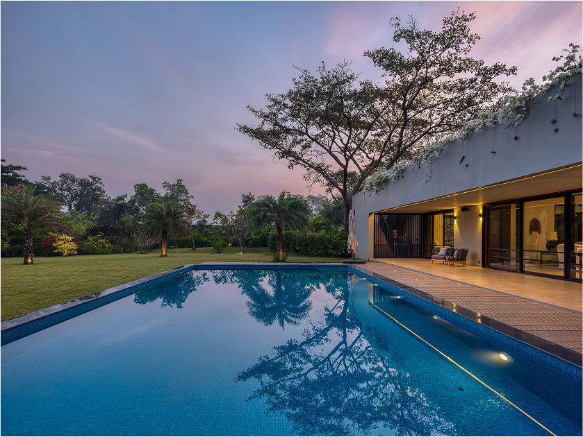 Luxury villa in Alibag with a swimming pool and lush green lawn at sunset.