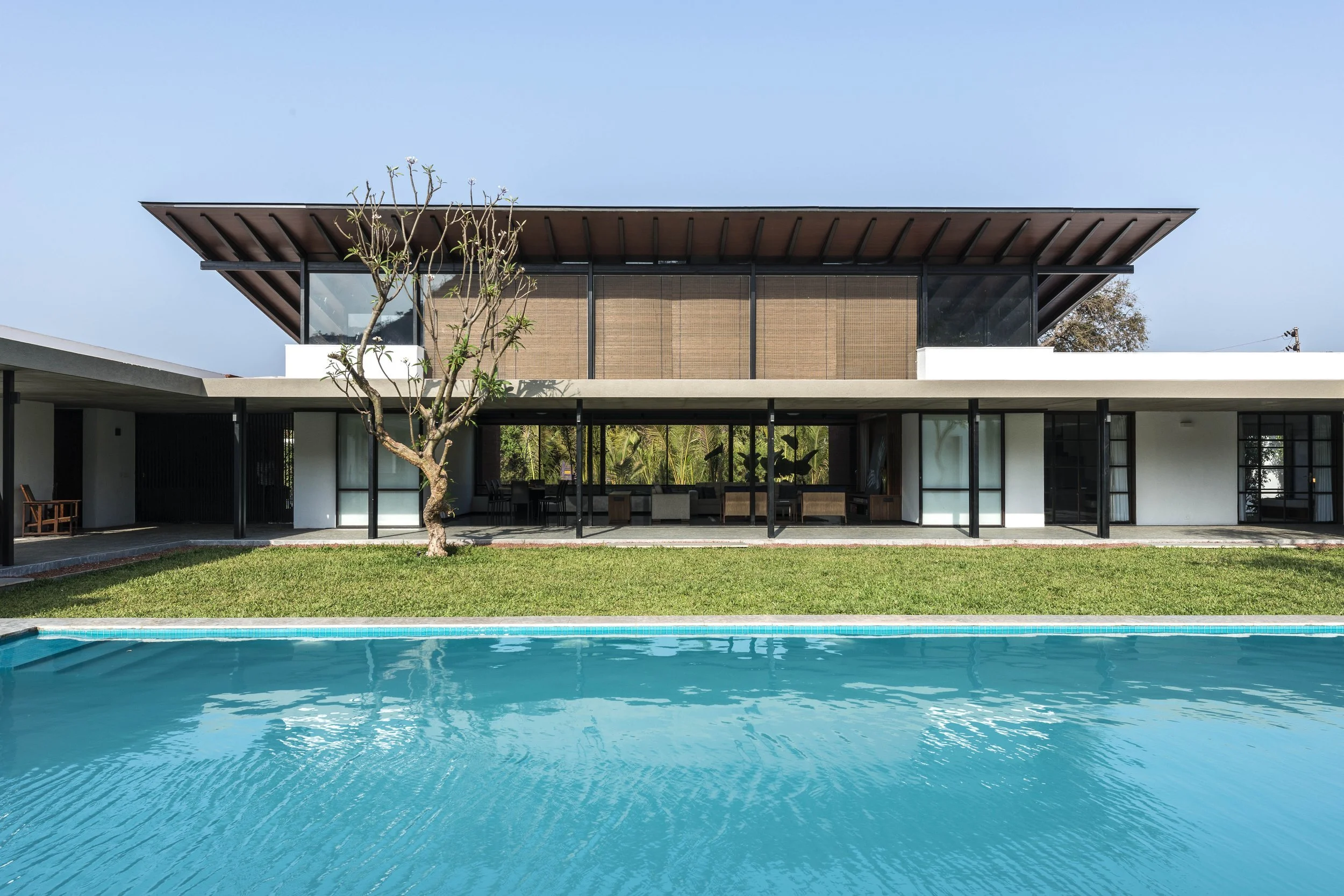 Modern two-story house with large windows, flat roof, pool in foreground, and lawn