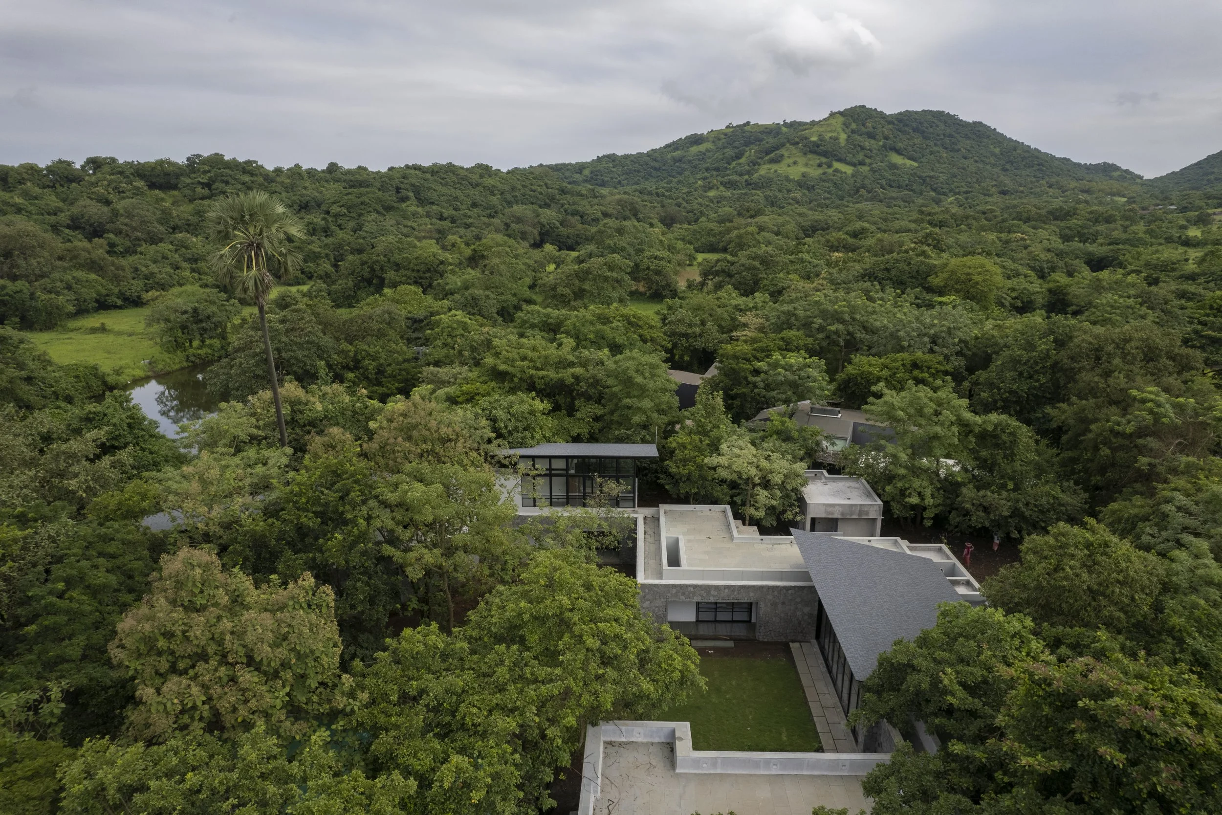 Aerial view of a modern house surrounded by a dense forest with a mountain in the background.
