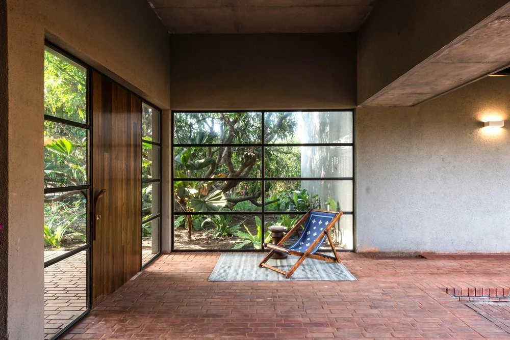 Modern interior with large glass windows, wooden door, brick flooring, and a folding chair with a side table.