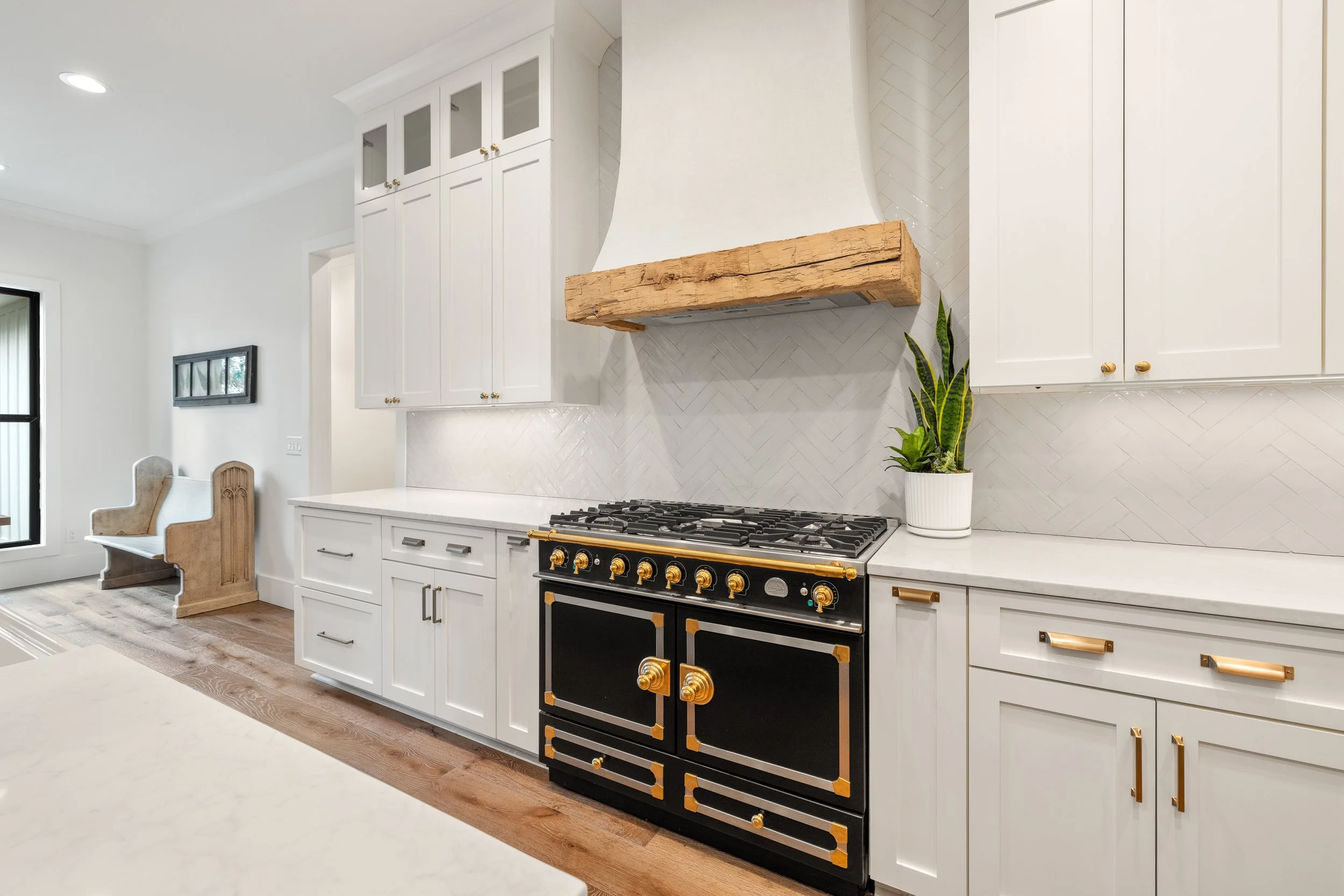 Custom cabinetry. Custom site built arched stucco coated hood vent with reclaimed wood detail. Quartz counters with tile backsplash installed on herringbone pattern.