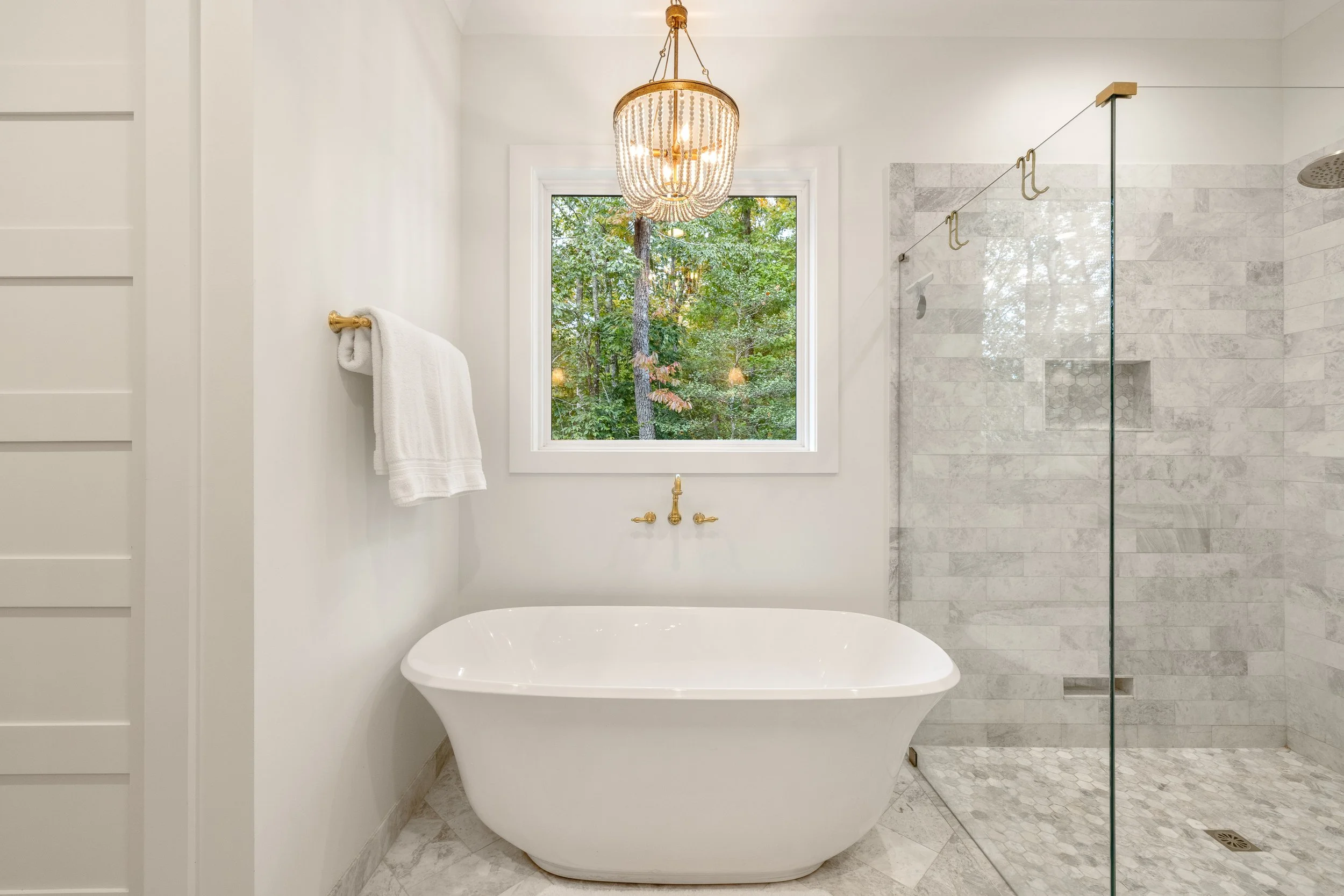 Freestanding tub with wall mount tub faucet. Curbless custom tile shower with frameless glass shower walls. Marble tile on walls and floor.