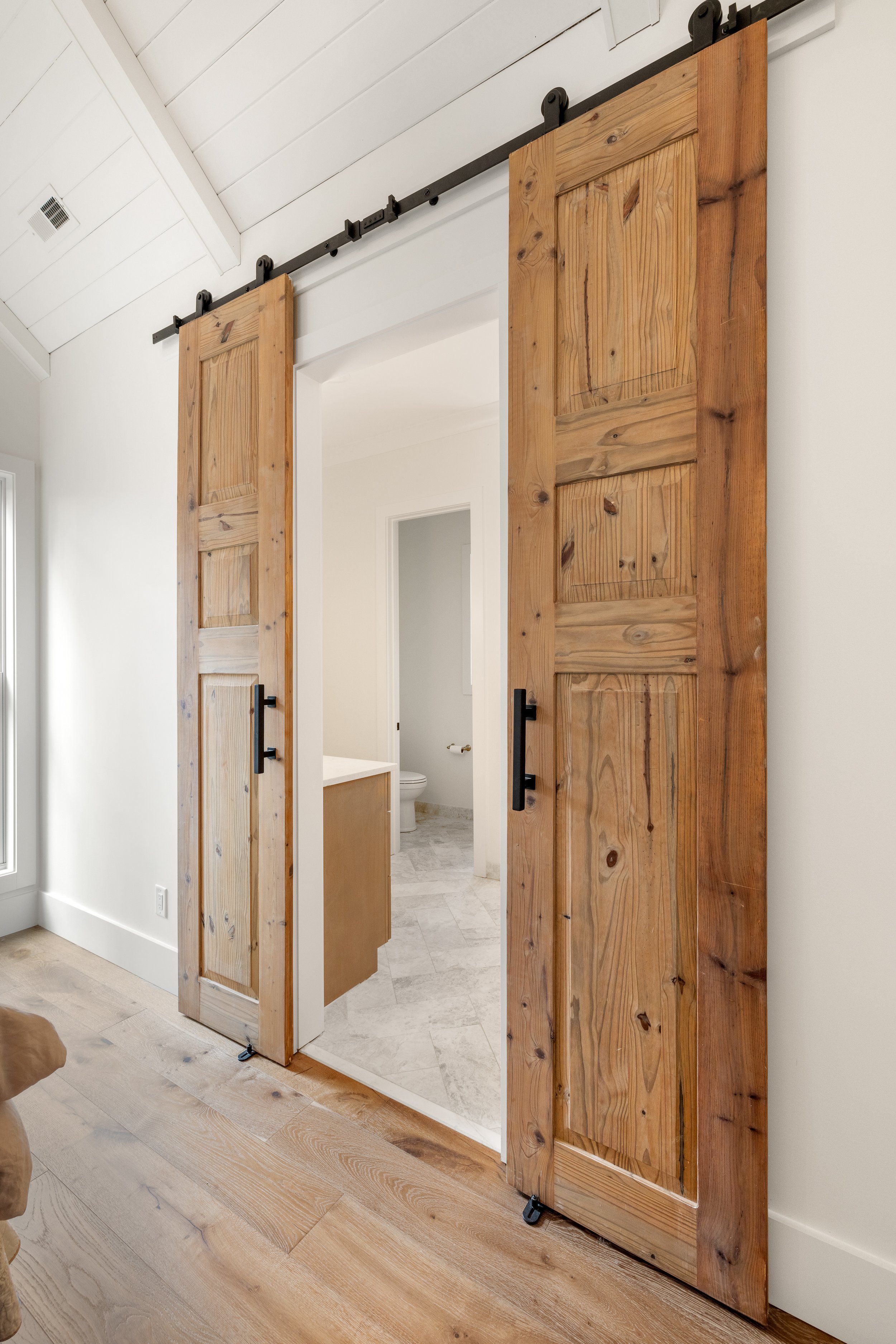 Custom double barn doors leading from primary bedroom into primary bathroom.