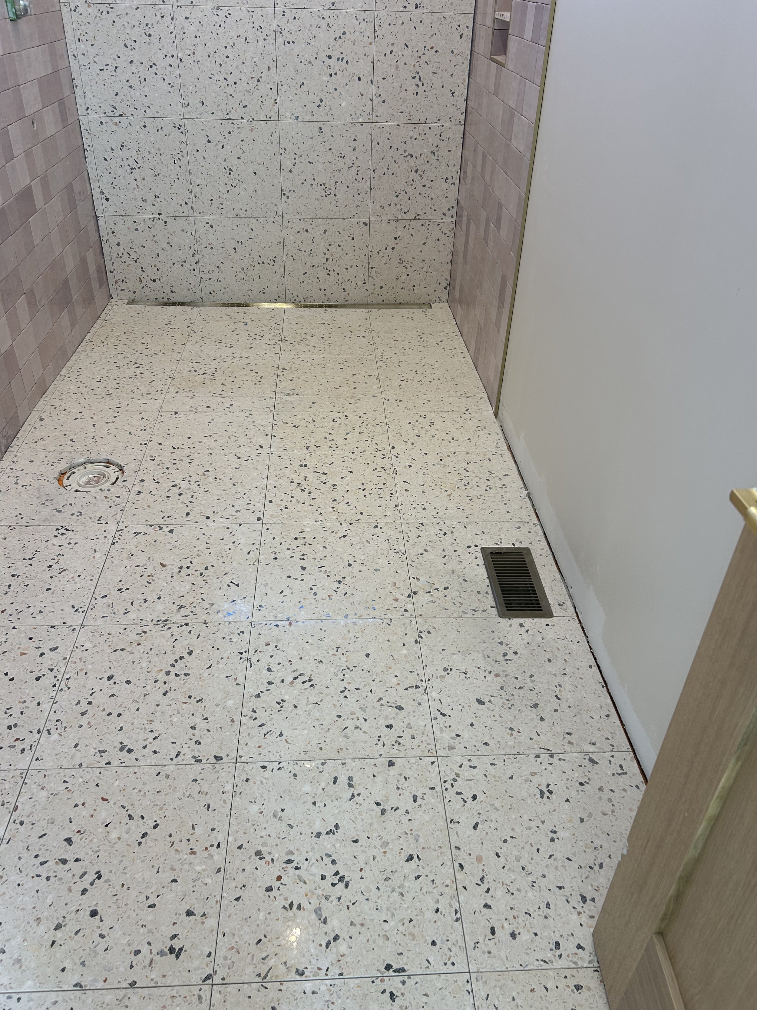  16"x16" real terrazzo tiles installed on floor and back wall of bathroom and shower. Curbless shower entry with gold trench drain against wall.