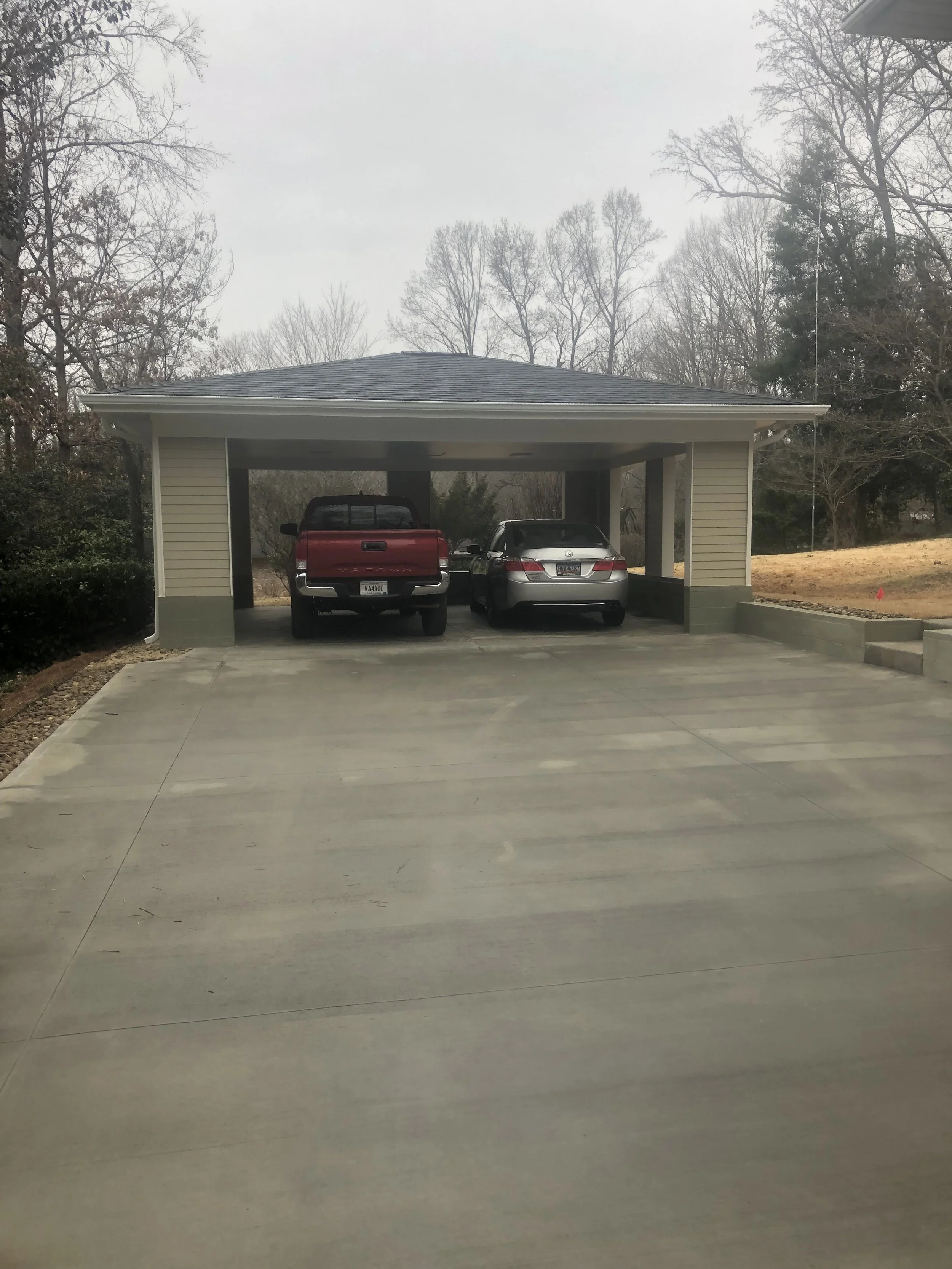 Detached carport with a shallow hip roof. Fiber cement plank siding and asphalt architectural shingles.