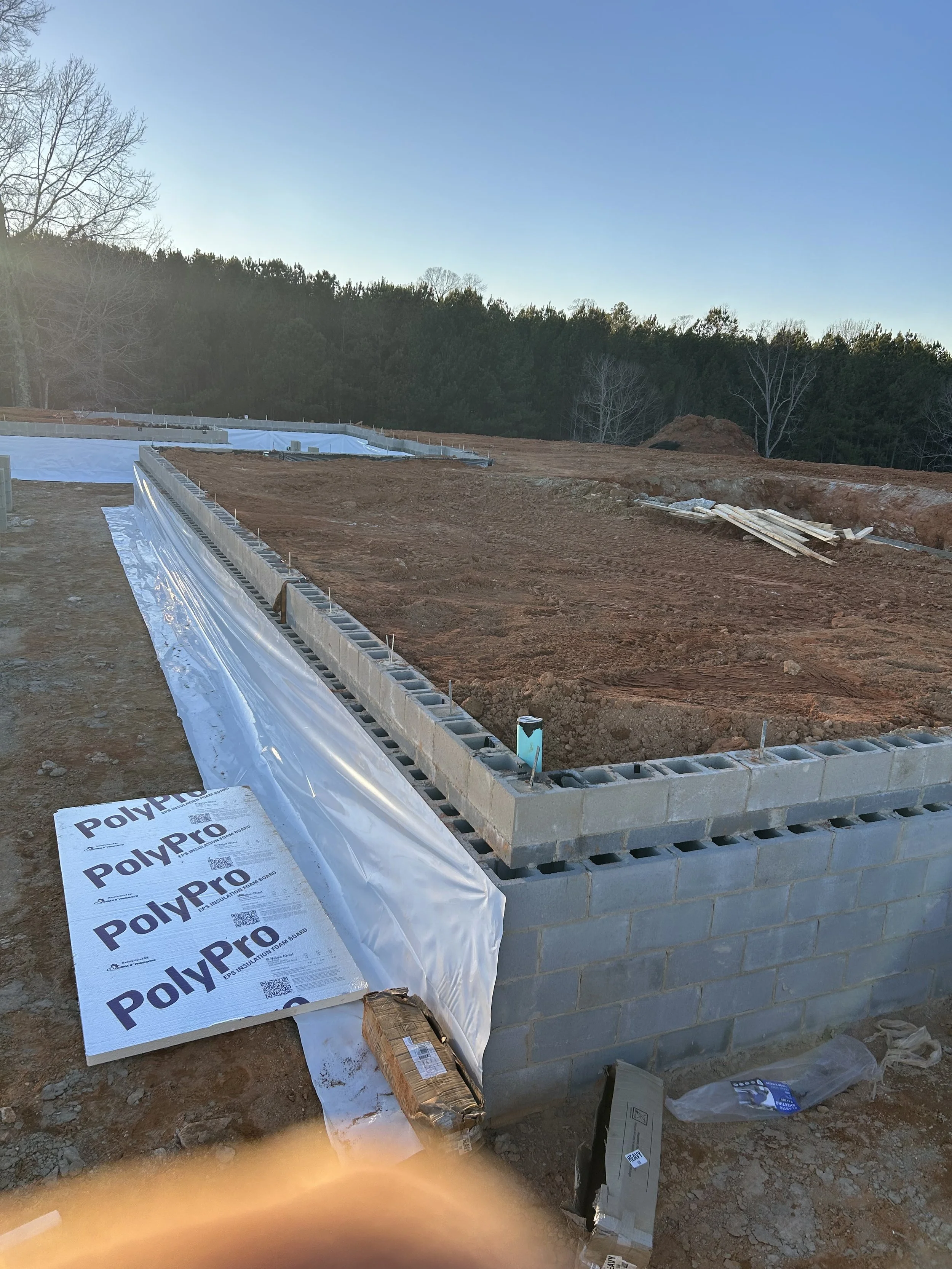 20mil poly installed on walls for beginning of crawlspace encapsulation. 4" drainage pipe placed in area for future downspout. Foundation backfilled against.