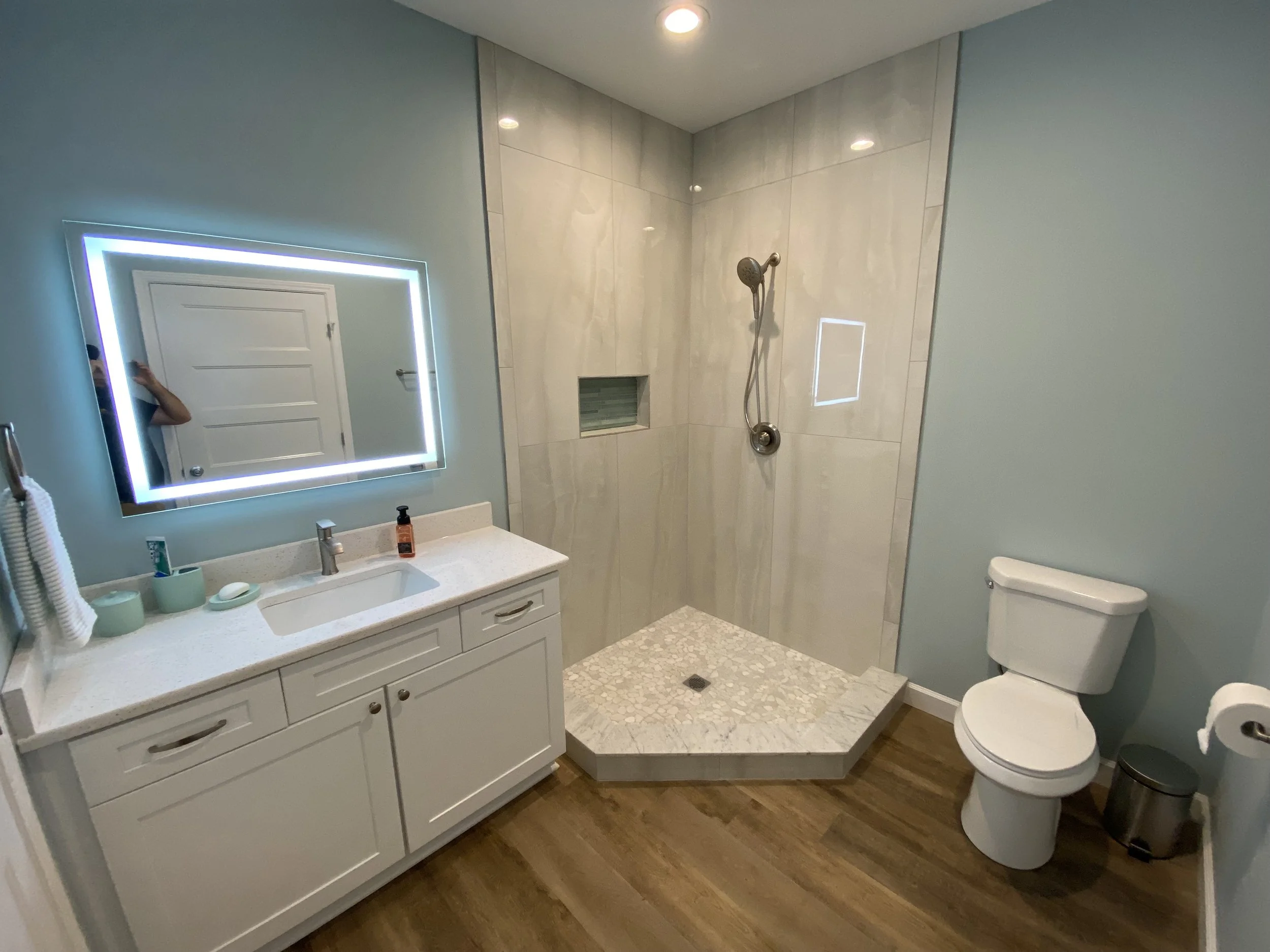 Full bathroom in detached studio apartment/pool house. LVP flooring. Semi custom vanity cabinet with Quartz top. Light up vanity mirror. Custom tile corner shower.