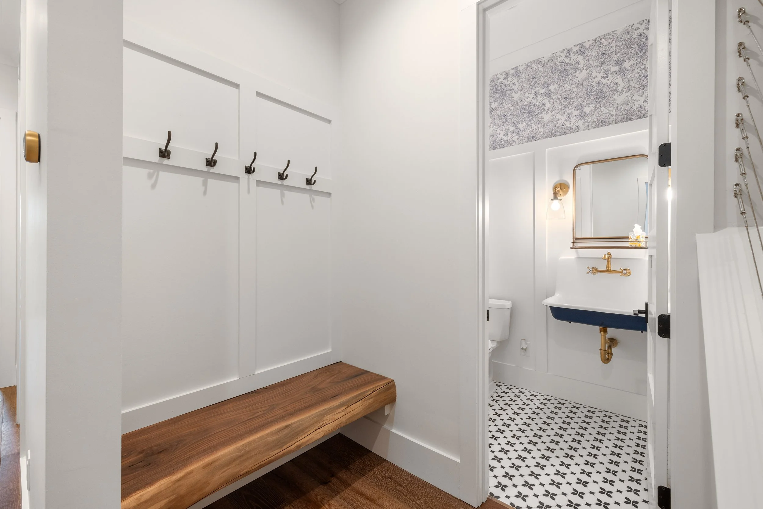 Custom 5"x16" wood bench with live edge. Half bath with pattern tile and a wall mount sink. Coat hooks mounted above bench.