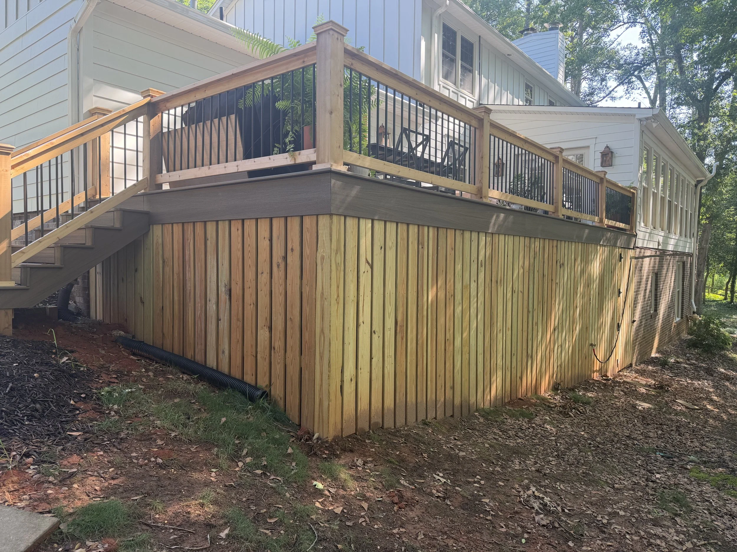 Trex Enhance Naturals composite decking and matching composite skirt board. Pressure treated vertical wood slat underpinning.