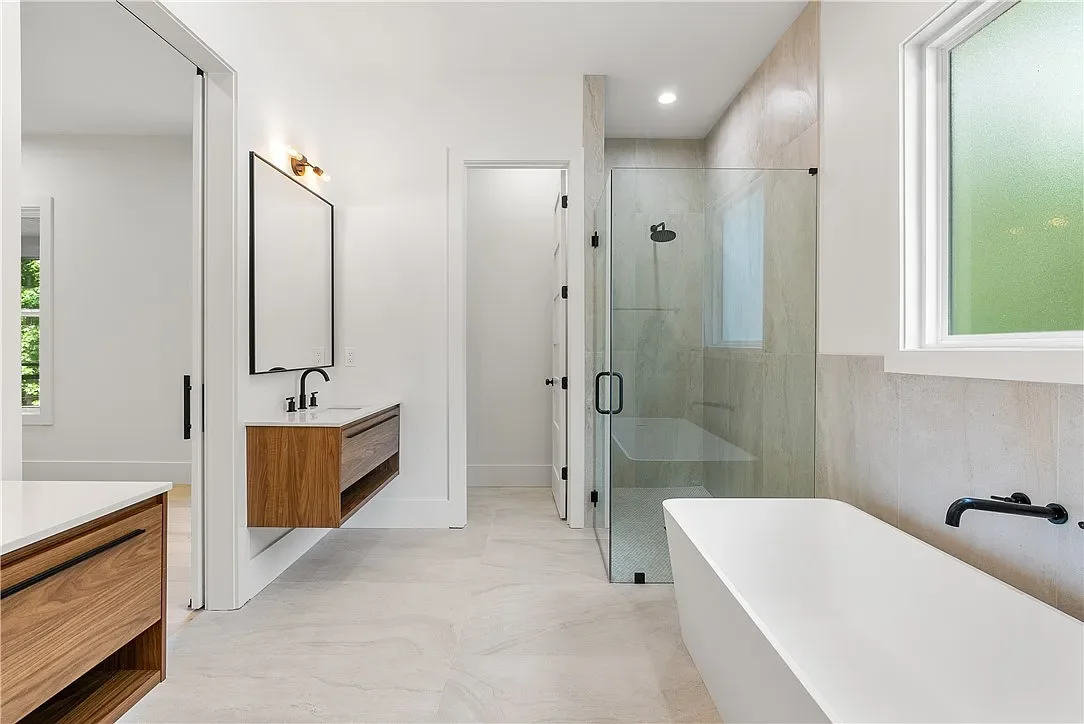 Large format tile on primary bathroom floor, shower walls and behind freestanding tub. Custom curbless entry tile shower with frameless glass shower wall.