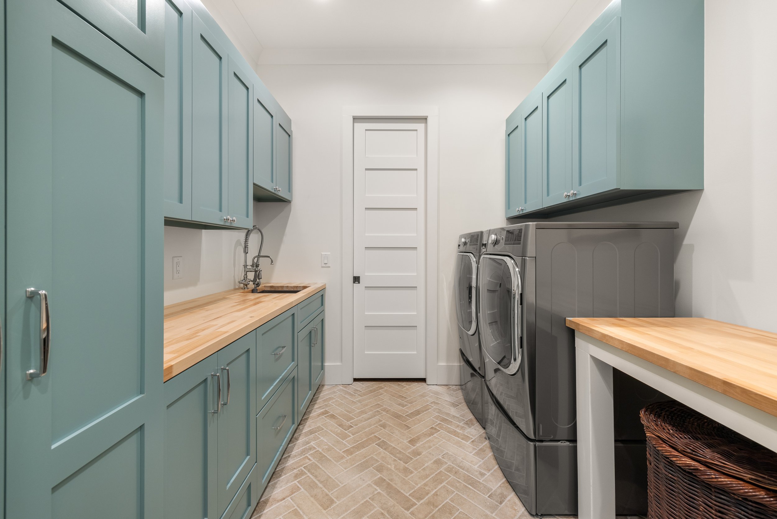 Dual entry laundry room with custom cabinetry, butcher block counters, and brick paver tiles installed on a herringbone pattern.