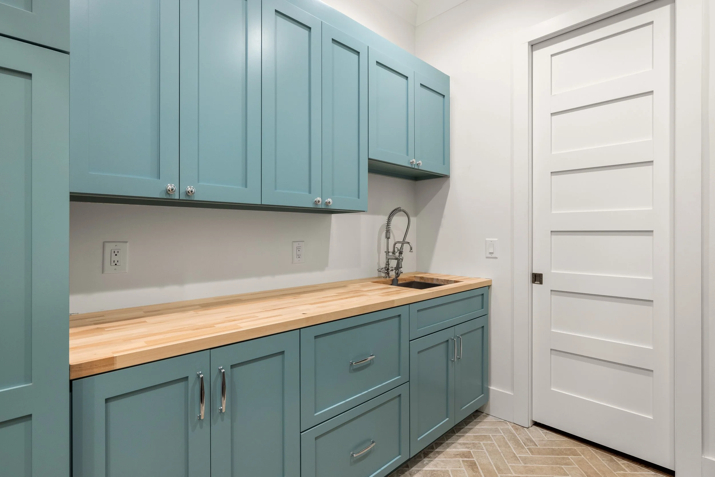 Dual entry laundry room with custom cabinetry, butcher block counters, and brick paver tiles installed on a herringbone pattern. 8' tall solid core doors.