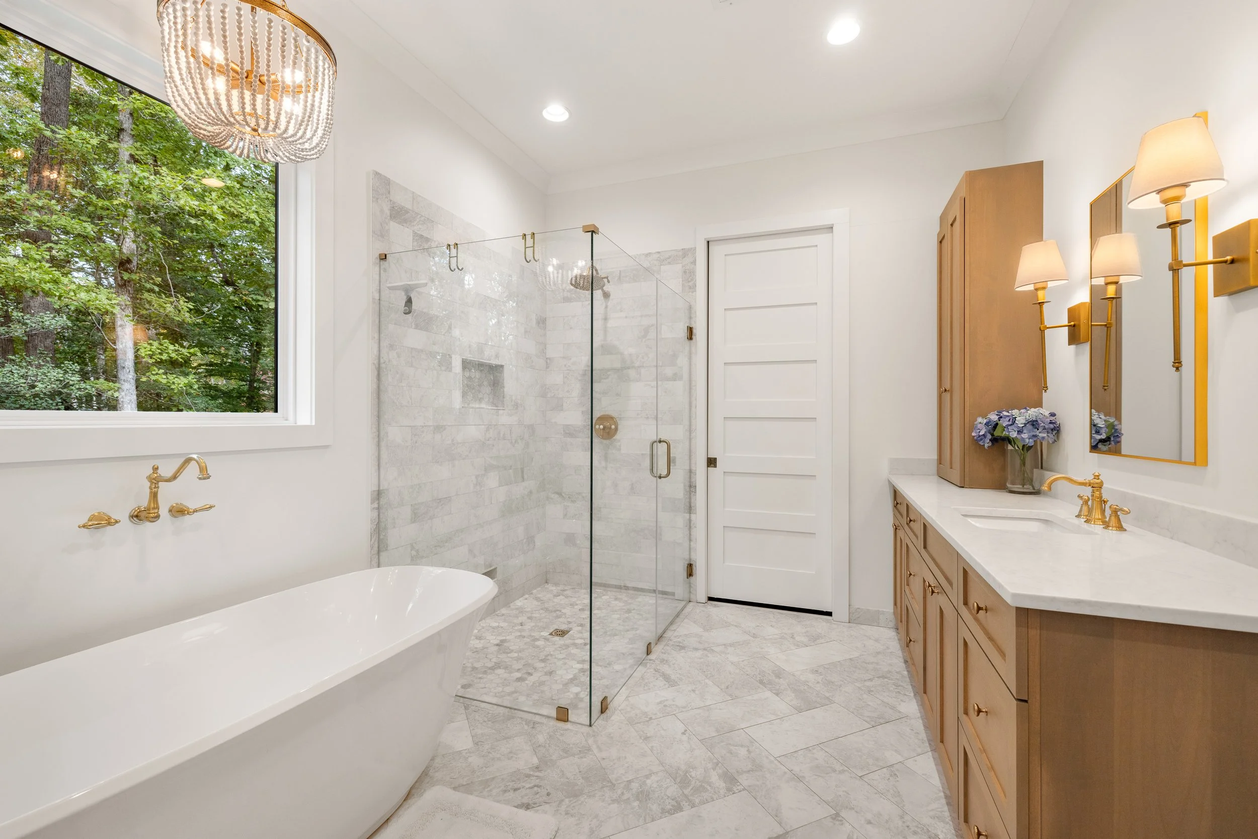 Freestanding tub with wall mount tub faucet. Curbless custom tile shower with frameless glass shower walls. Marble tile on walls and floor. 