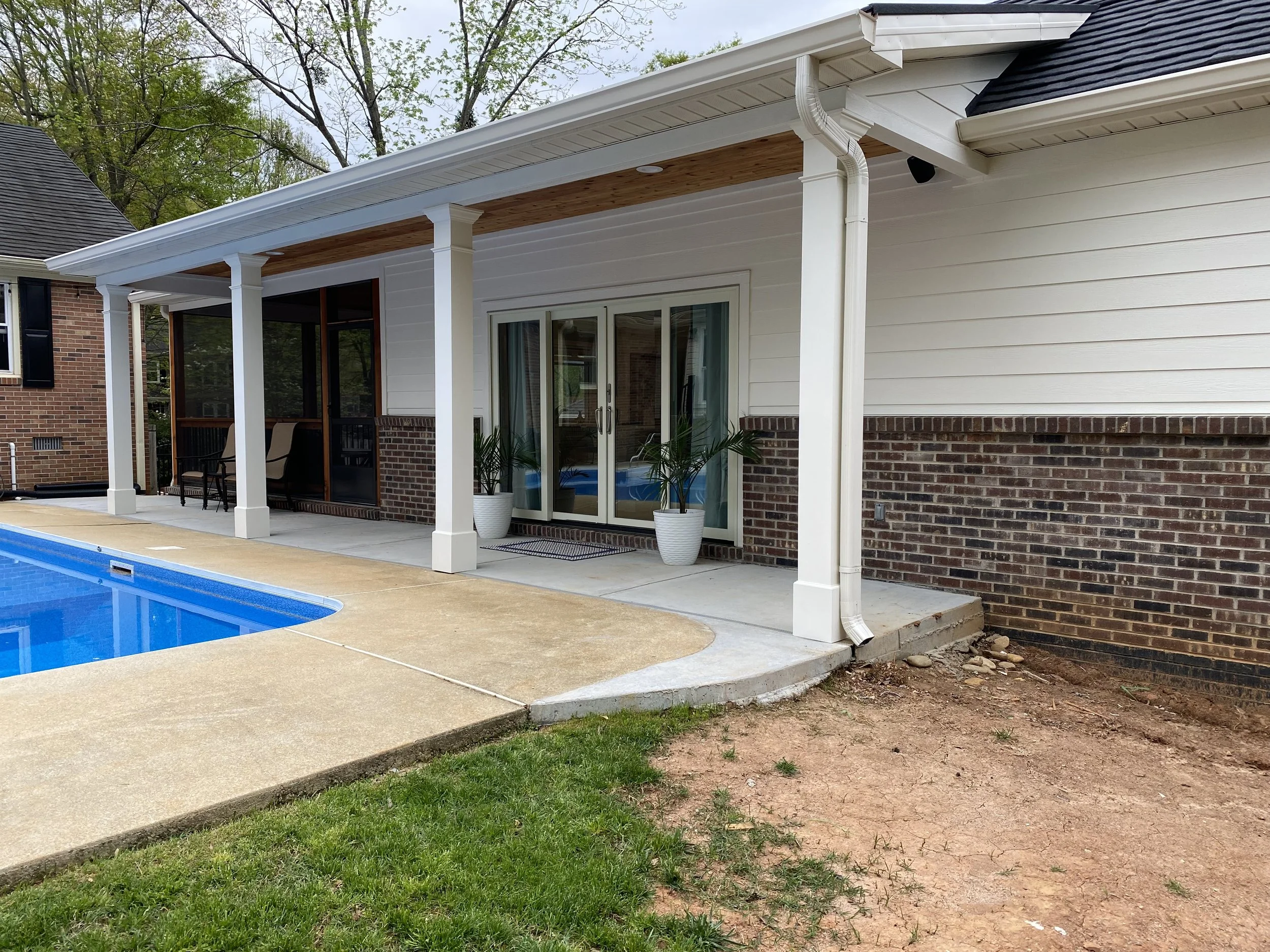 Front side of detached pool house/mother-in-law suite beside pool. Decorative PVC columns. Brick veneer and fiber cement siding. Aluminum shingle roofing with asphalt coating. Aluminum clad four panel bi parting sliding door.