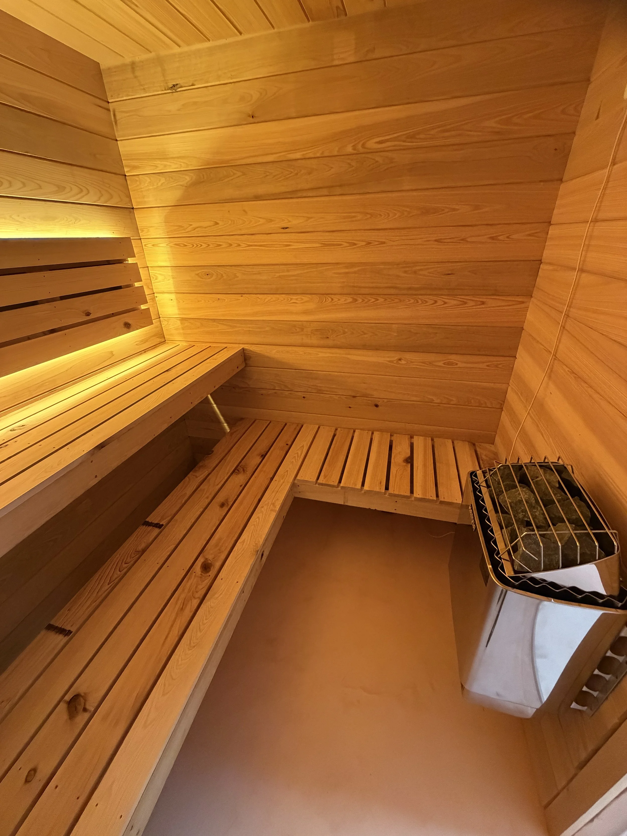 6'x7'x7' custom shower room with Harvia WiFi heater. Walls, ceiling, and benches are cypress wood. Floor is micro cement.