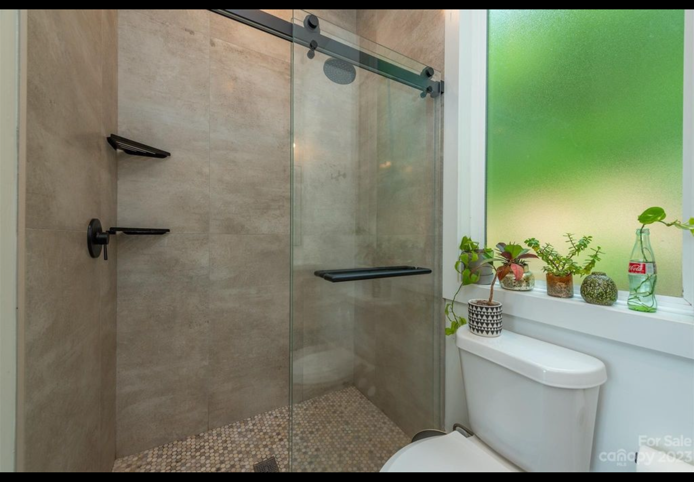 Curbless entry walk in custom tile shower with large format tiles on wall and penny tile on floor. Sliding glass shower doors. Obscure tempered glass vinyl picture window.