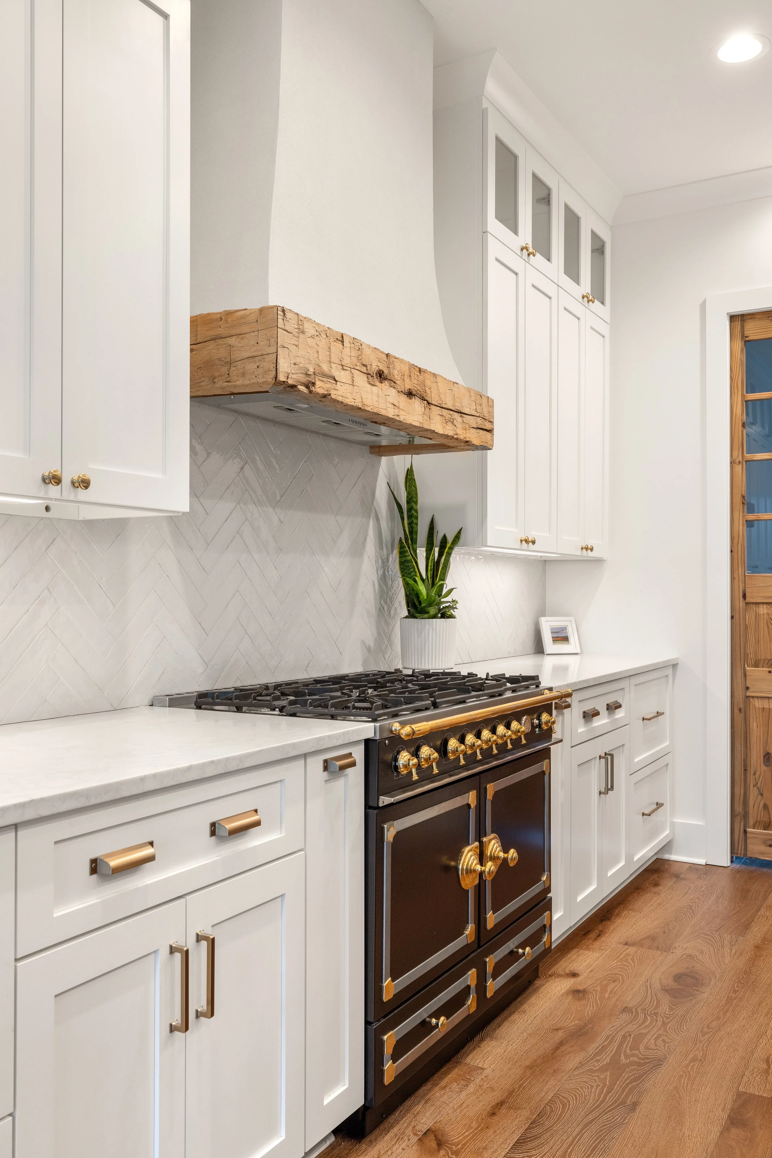 Custom cabinetry. Custom site built arched stucco coated hood vent with reclaimed wood detail. Quartz counters with tile backsplash installed on herringbone pattern.