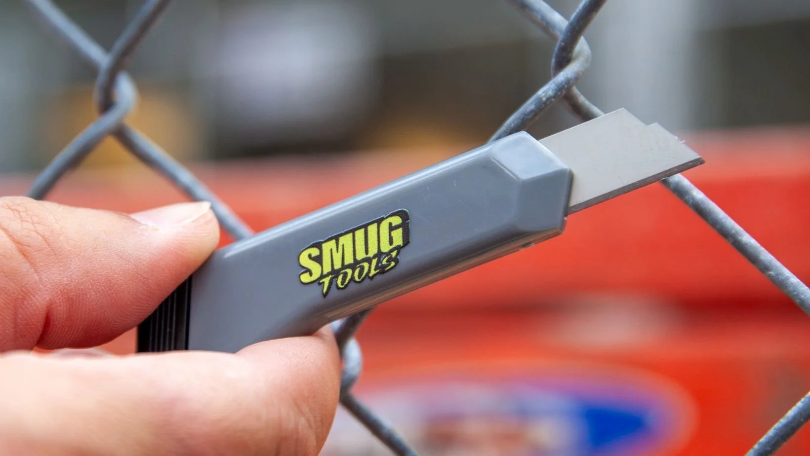 smug tools mini box cutter being held against chain link fence