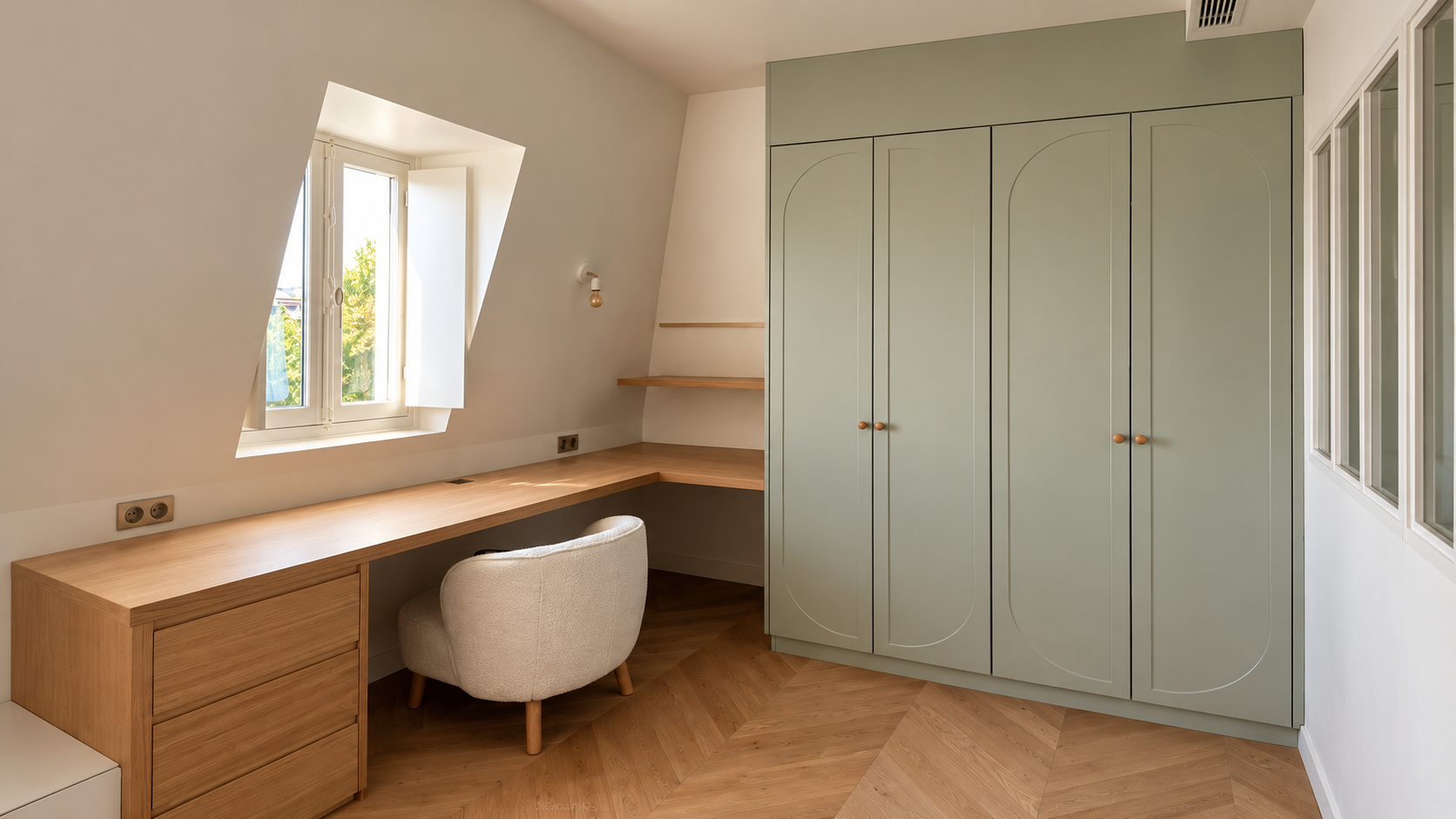 Bureau aménagé sous les combles avec bureau en bois, fauteuil beige, étagères et grande armoire vert sauge.