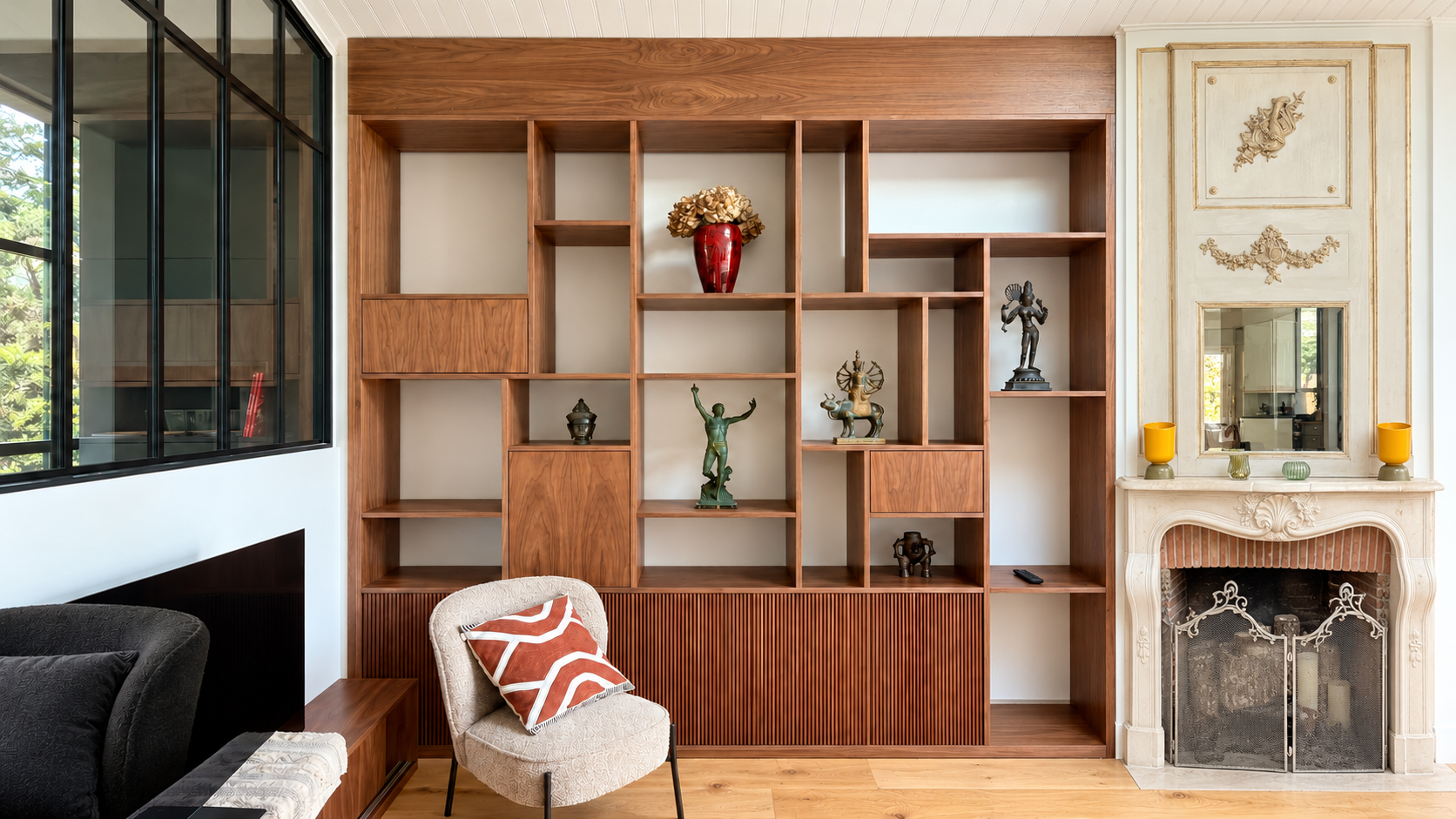 Intérieur d'un salon avec bibliothèque en bois, cheminée en marbre, fauteuil beige avec coussin à motifs, et décorations diverses.