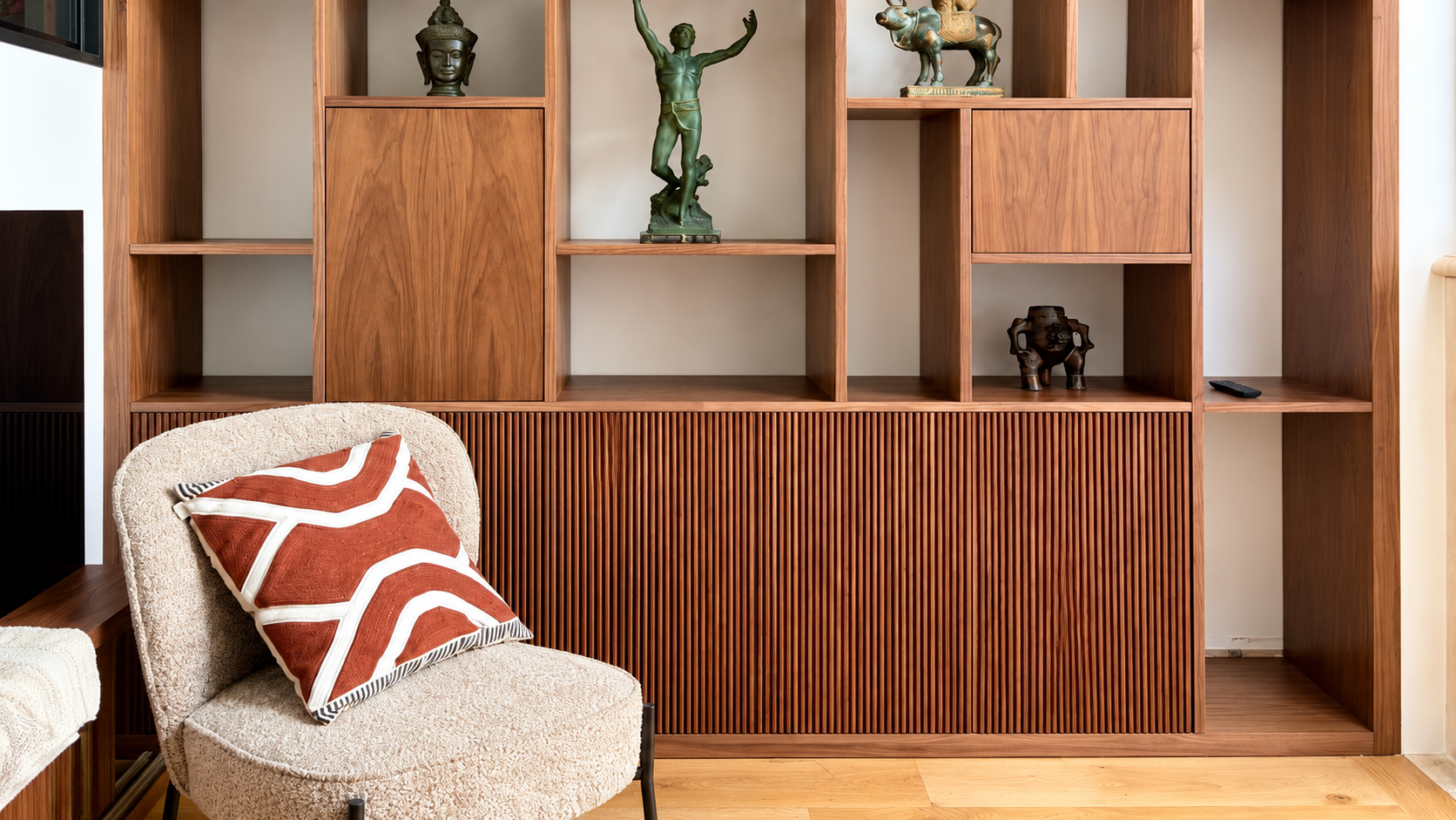 Une étagère en bois avec plusieurs figurines et objets décoratifs, une chaise avec un coussin à motifs, et un sol en bois.