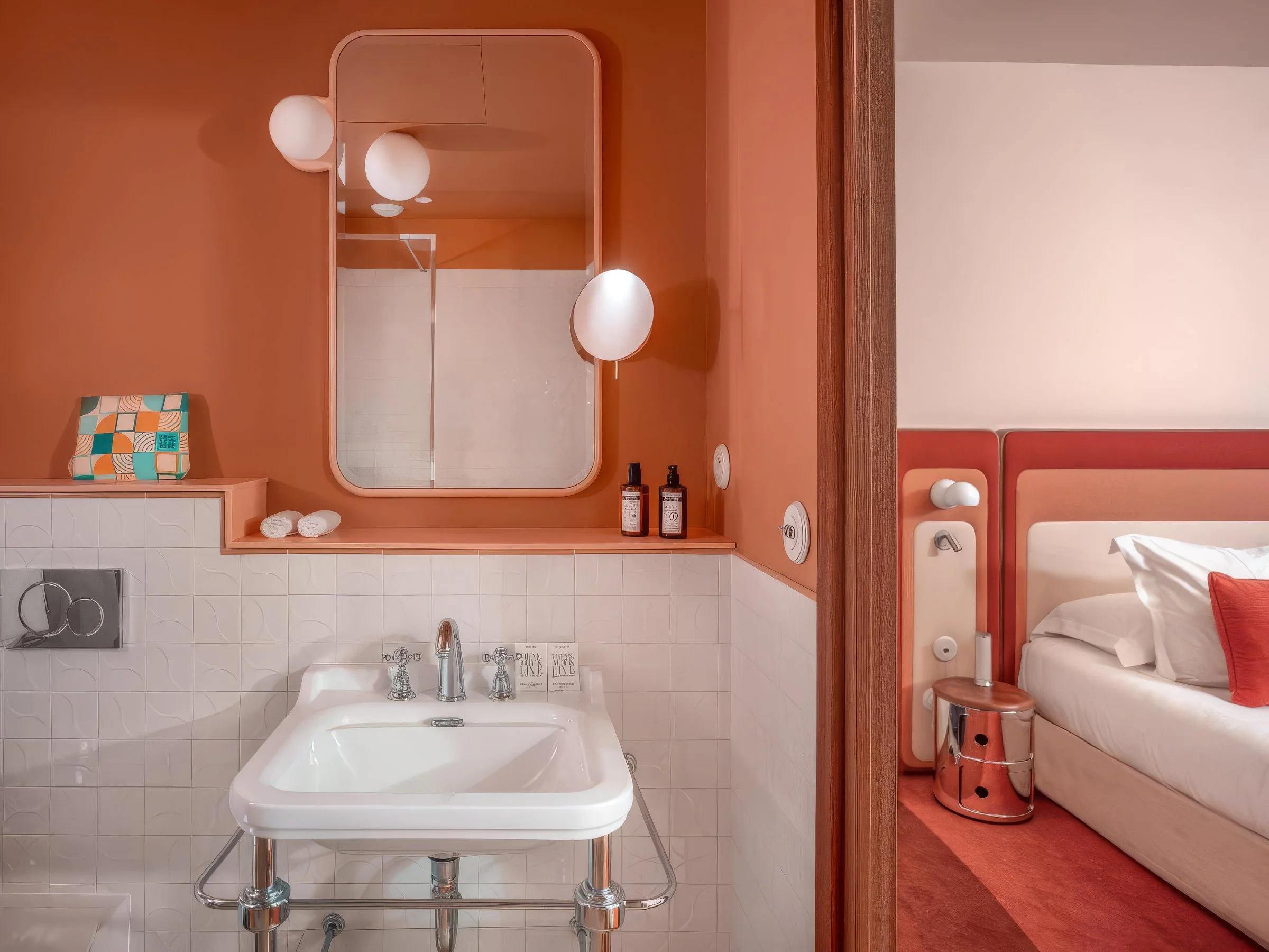 Une salle de bain avec un lavabo blanc, miroir rectangulaire, et un lit avec une tête de lit dans une chambre Adjacent. Couleurs chaudes avec murs orange et mobilier en bois.