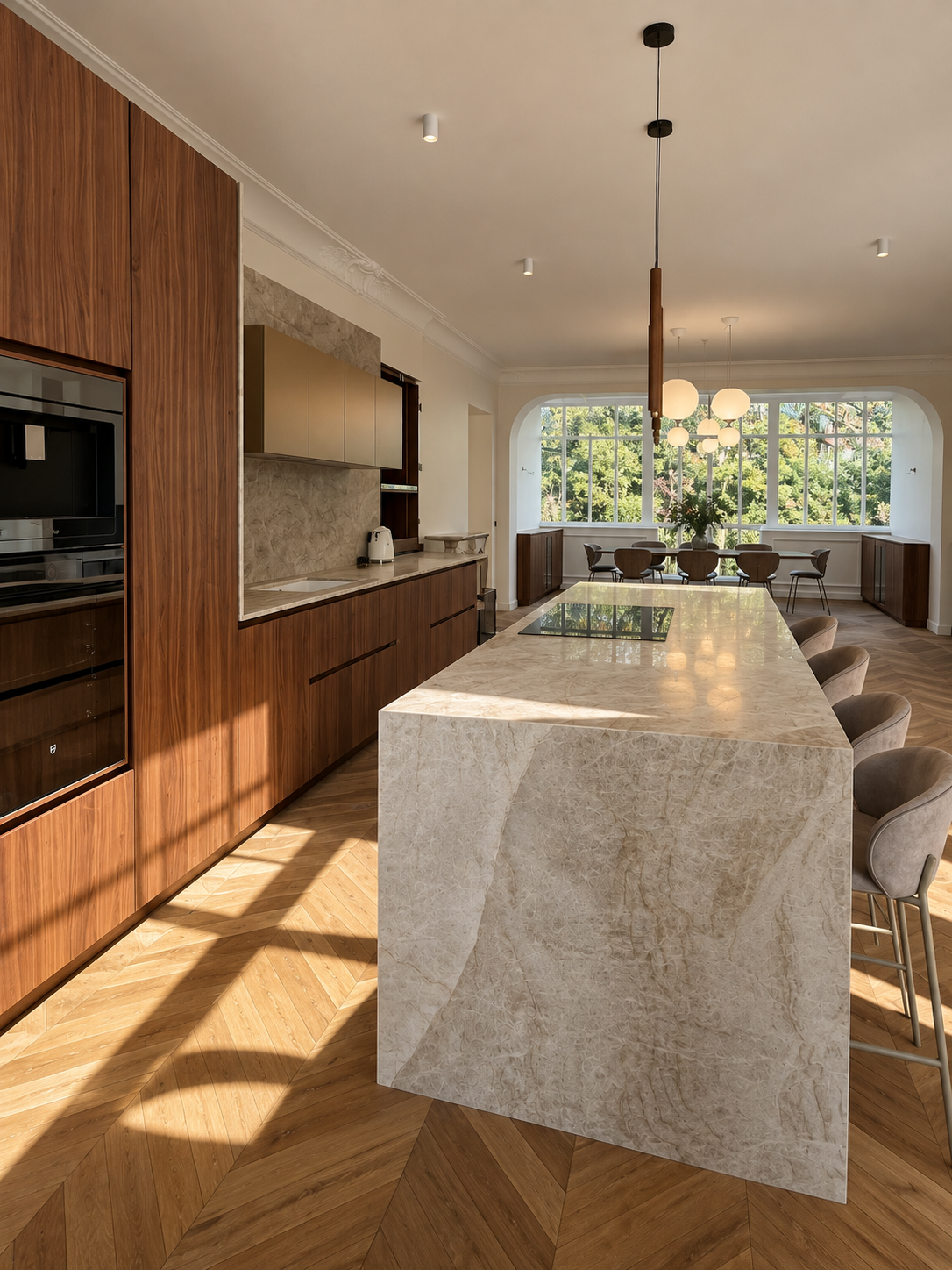 Cuisine moderne avec plan de travail en pierre beige, armoires en bois foncé, grande table en pierre, chaises en tissu beige, large fenêtre avec vue sur des arbres, luminaires suspendus, sol en bois parquet.