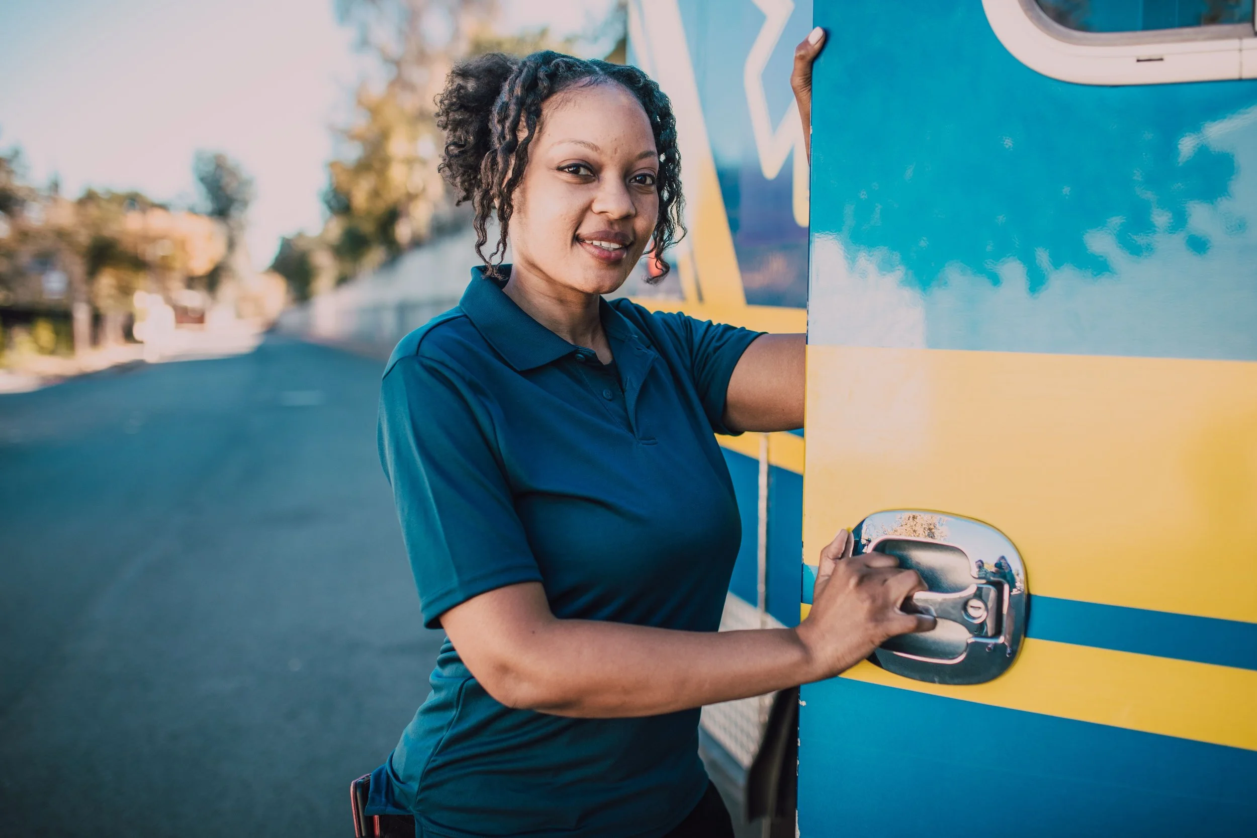 Smiling female bus driver opening the door of a colorful city bus