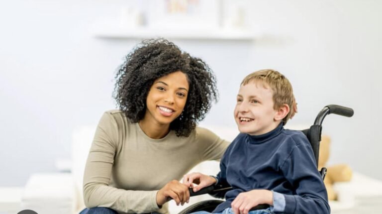 Woman and boy in a wheelchair smiling and holding hands indoors.