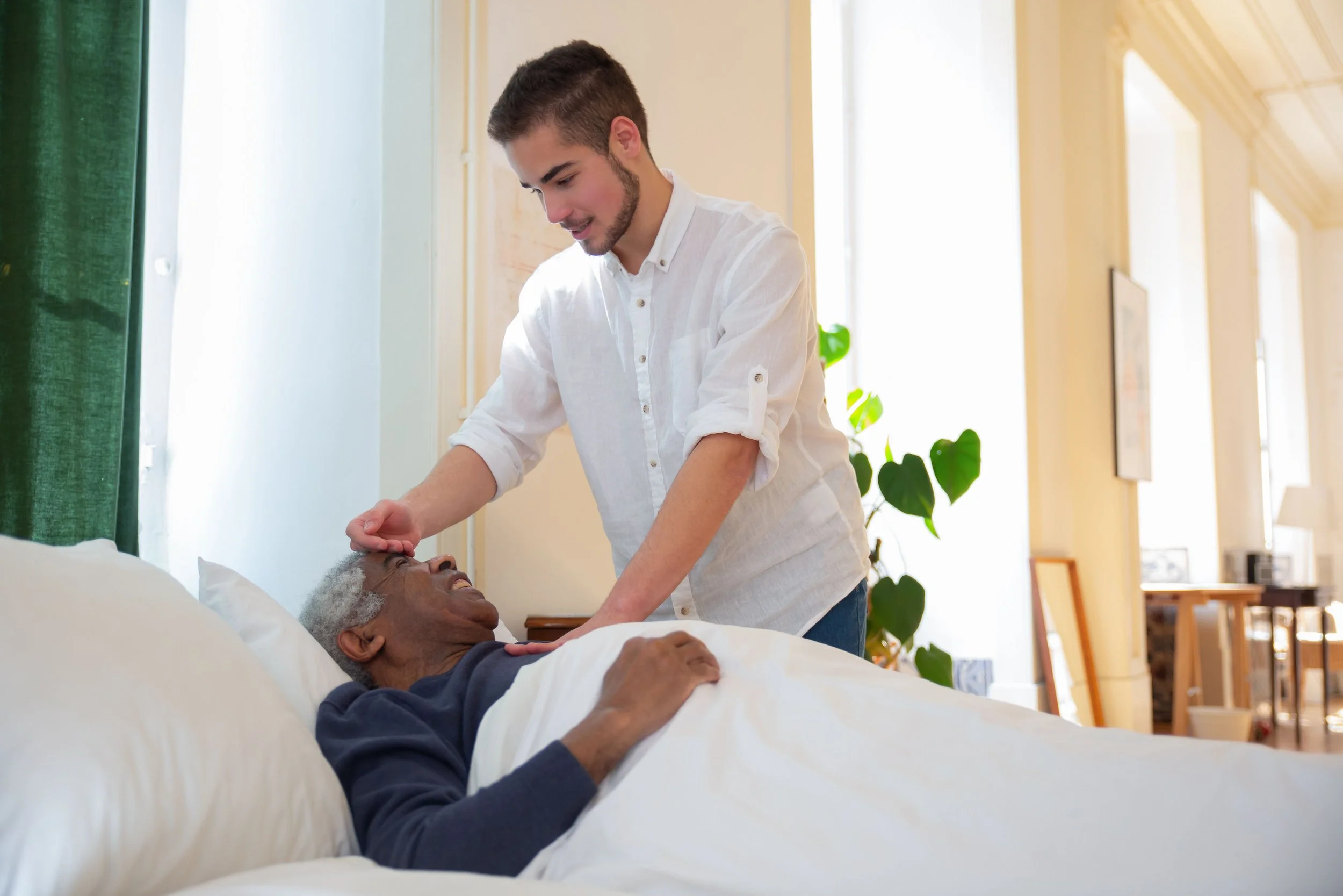 Caregiver helping an elderly man relax in bed at home