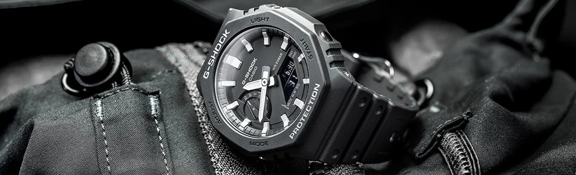Black G-Shock watch resting on a black tactical backpack with zippers.