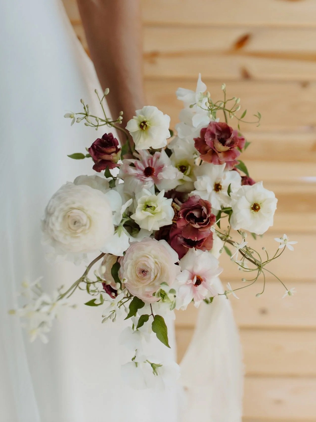 A bouquet of white, pink, and burgundy flowers against a wooden background.