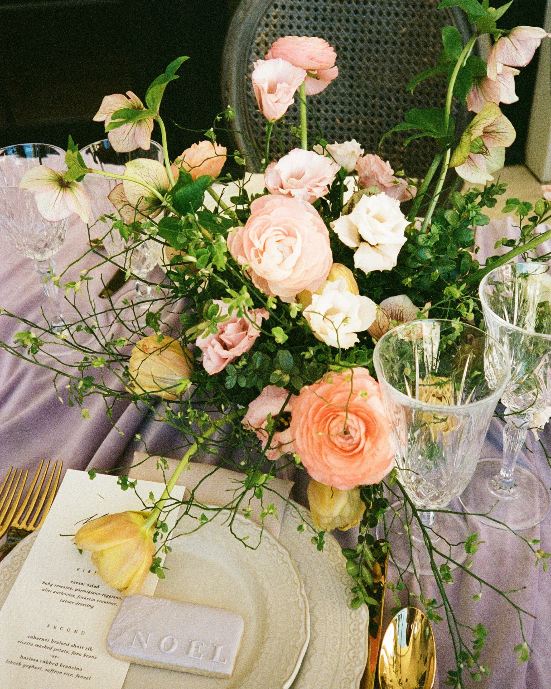 Elegant table setting with a floral centerpiece, gold utensils, crystal glasses, and a menu card on a purple tablecloth.