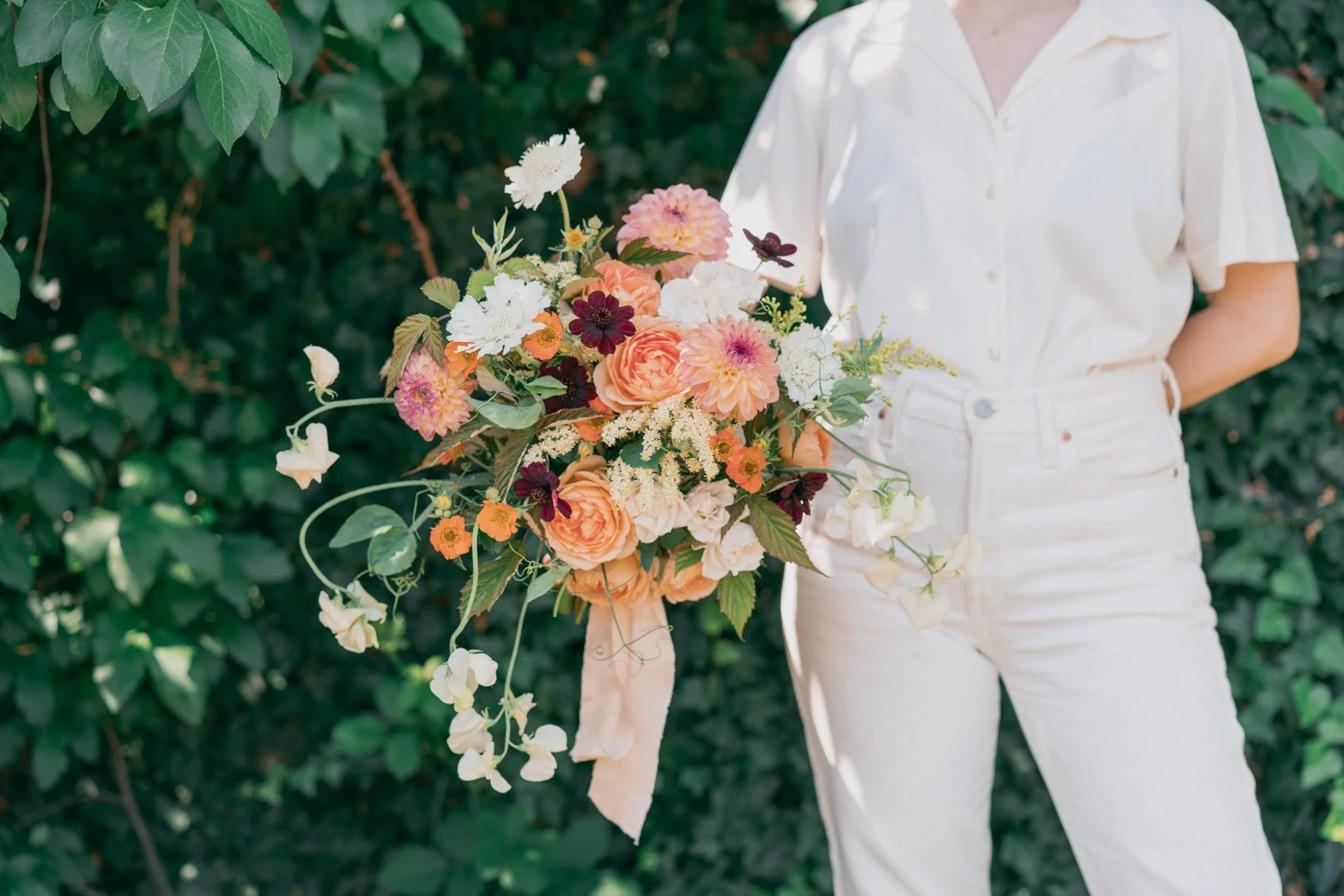Cascading summer bouquet with peach dahlias, garden roses, burgundy chocolate cosmos, white scabiosa, and trailing sweet peas, floral design by Faded Era Floral
