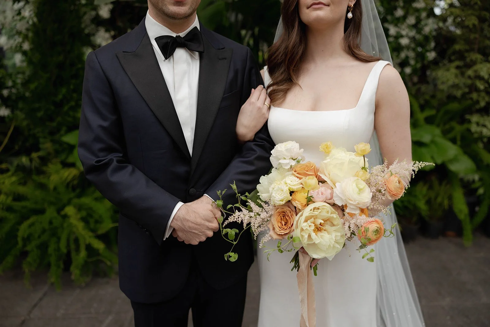 Bride and groom close-up at wedding in Minneapolis, Minnesota. Bride holding a lush garden-style bouquet of ivory garden roses, peach ranunculus, and yellow ranunculus with trailing greenery, floral design by Faded Era Floral.