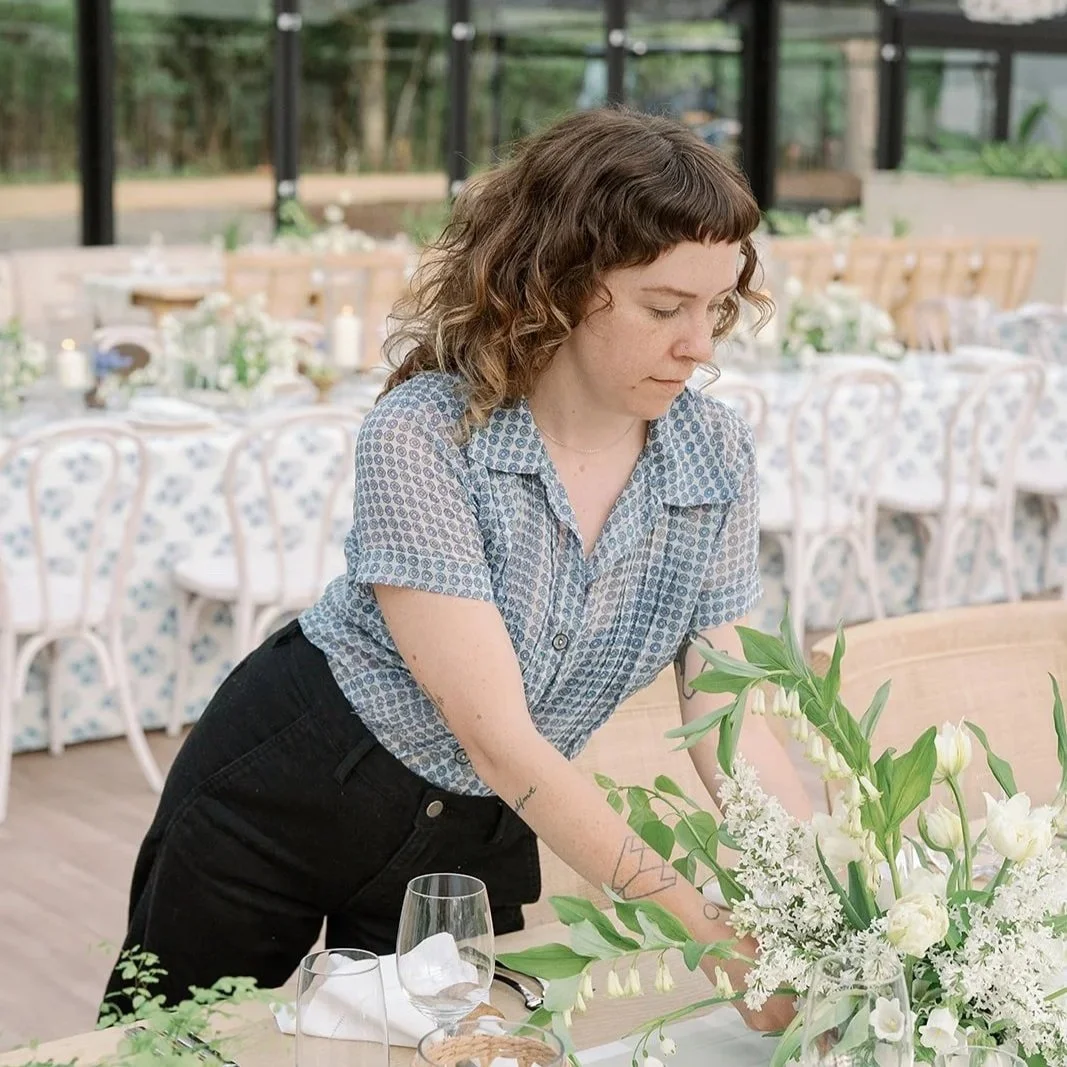 Woman arranging white flowers on a table in a decorated event space.