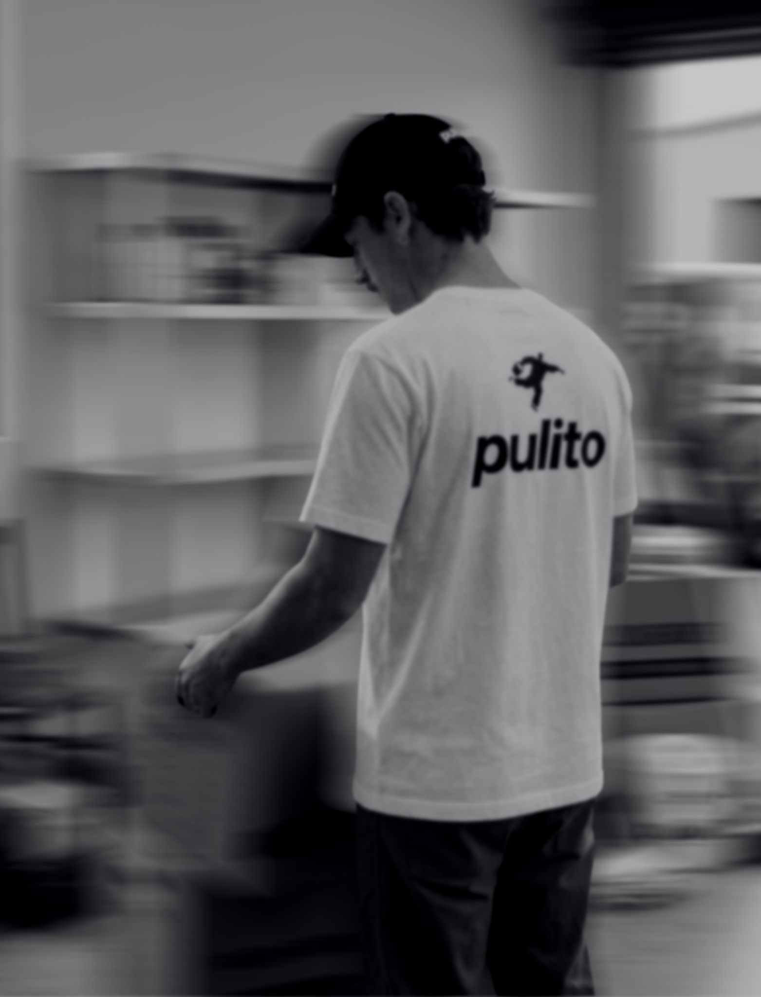 Person wearing a Pulito branded shirt walking inside a building with shelves.