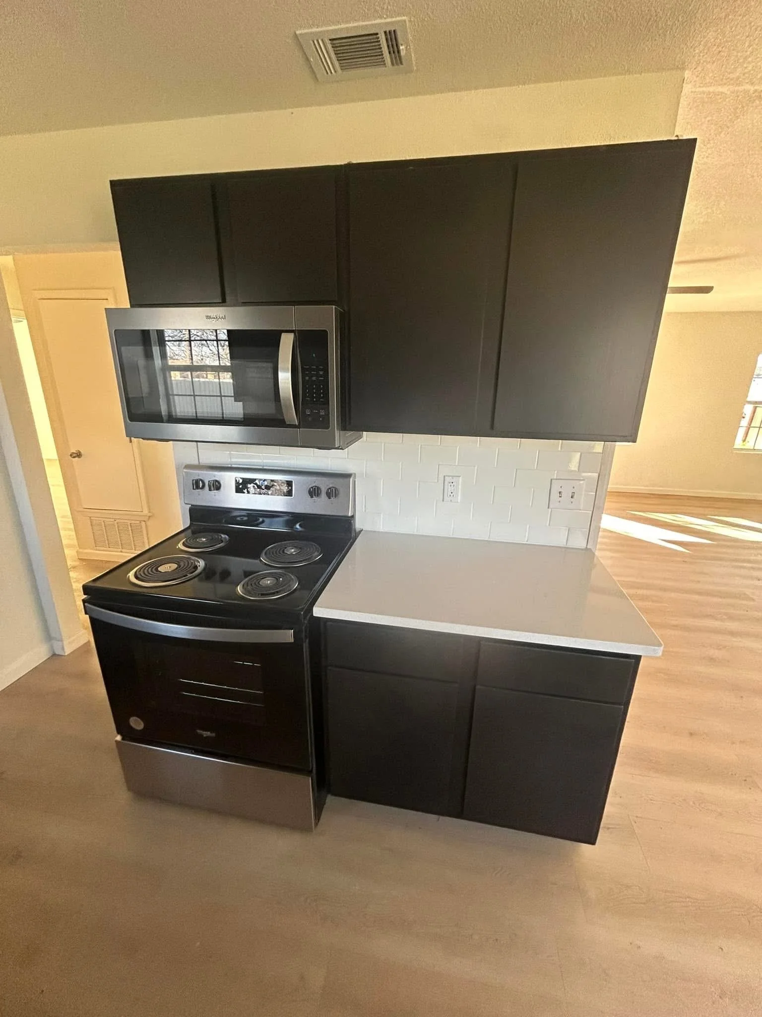 Kitchen with black cabinets, stainless steel microwave, black stove, white backsplash, and wooden flooring.