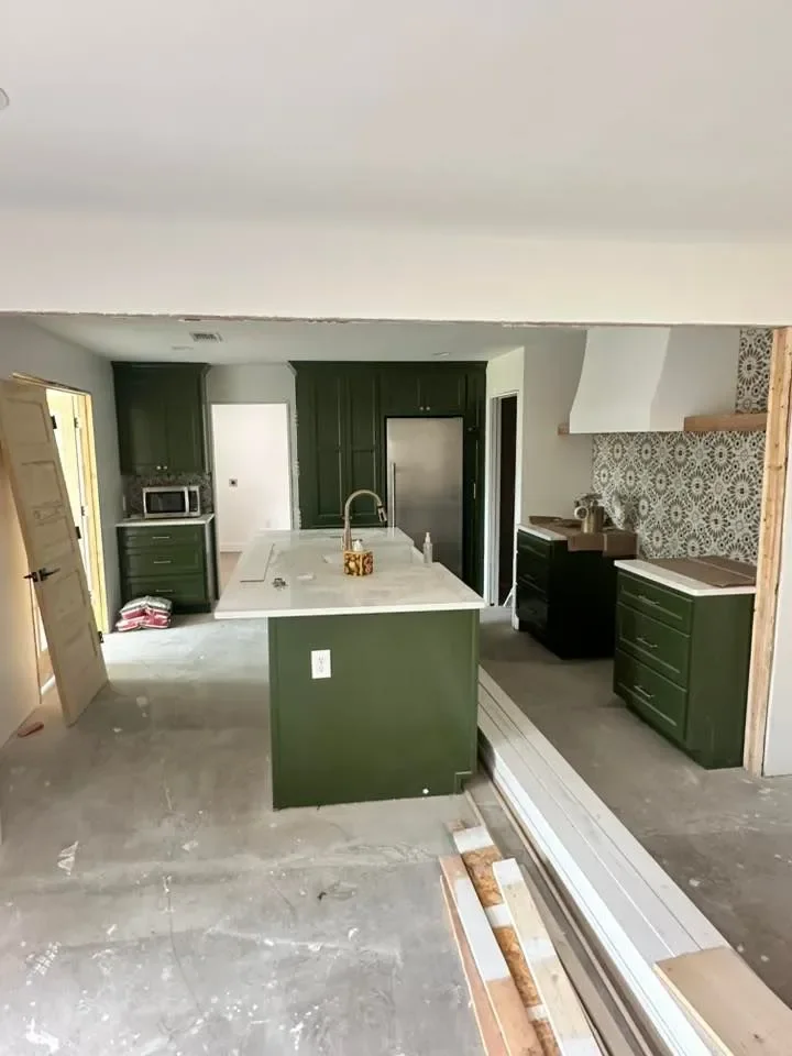 Kitchen under renovation with green cabinets, a white island with a sink, a microwave, a black oven, and a patterned backsplash.