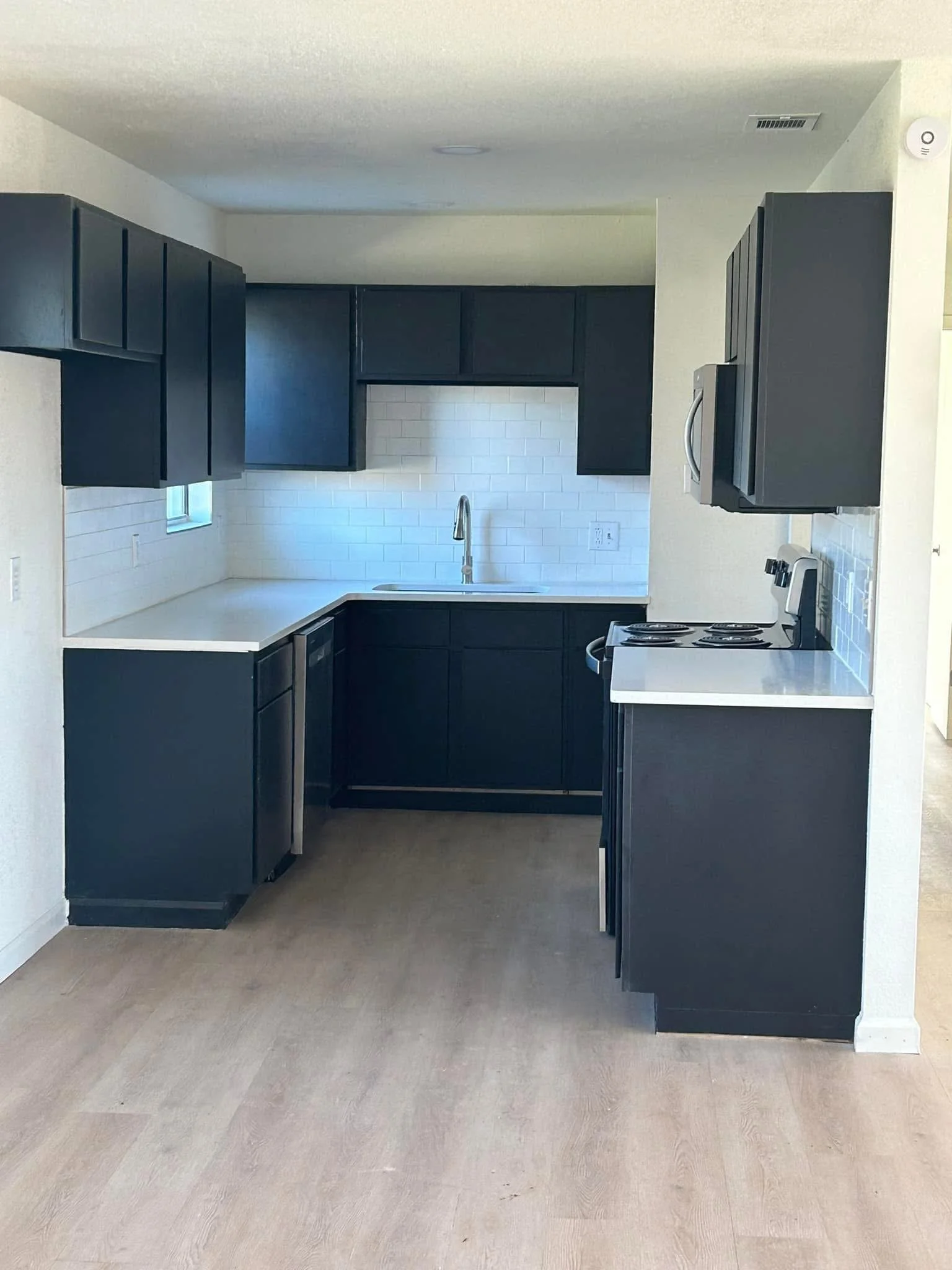 Empty kitchen with black cabinets, white countertops, white subway tile backsplash, and stainless steel appliances, including a microwave and stove.