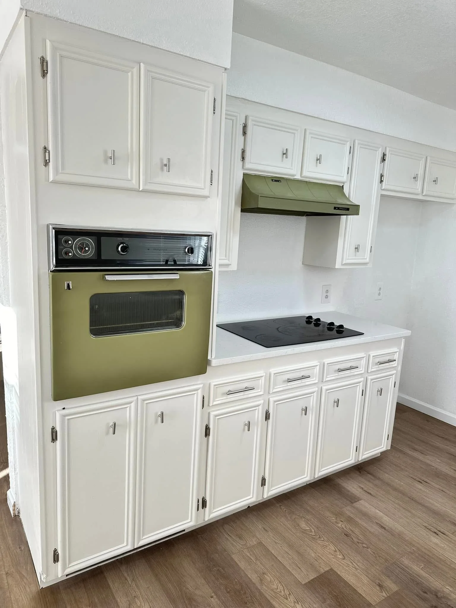 White kitchen cabinets with silver knobs beneath a white countertop and stovetop, with a green range hood above.