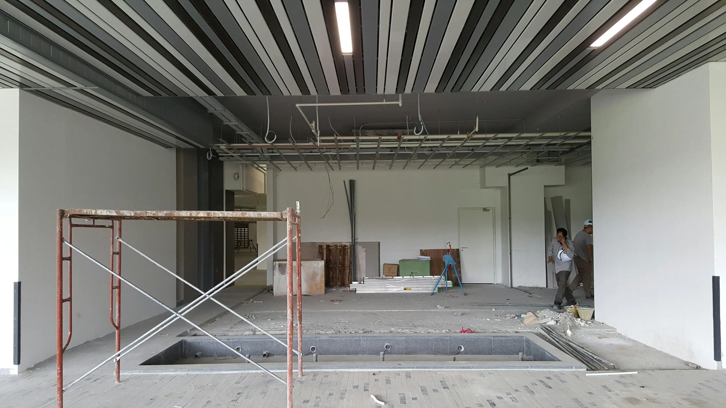 Construction workers inside an unfinished building, with scaffolding, exposed piping, and construction materials