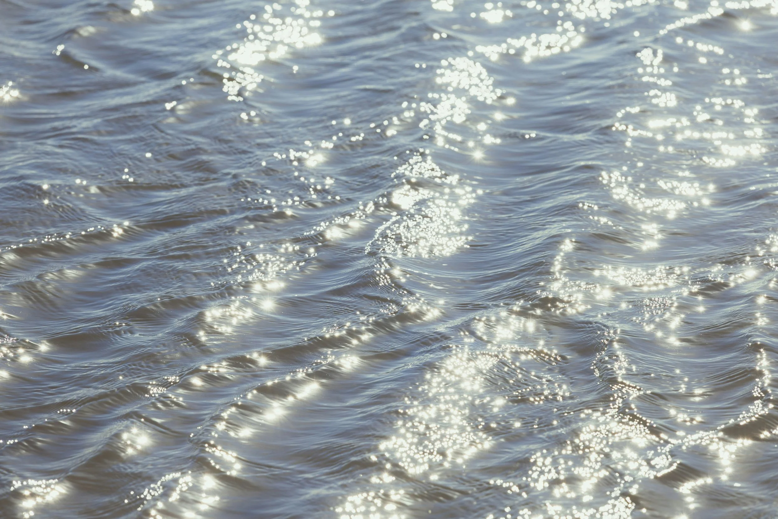 Sunlight reflecting off the surface of a body of water, creating bright sparkles and gentle ripples.