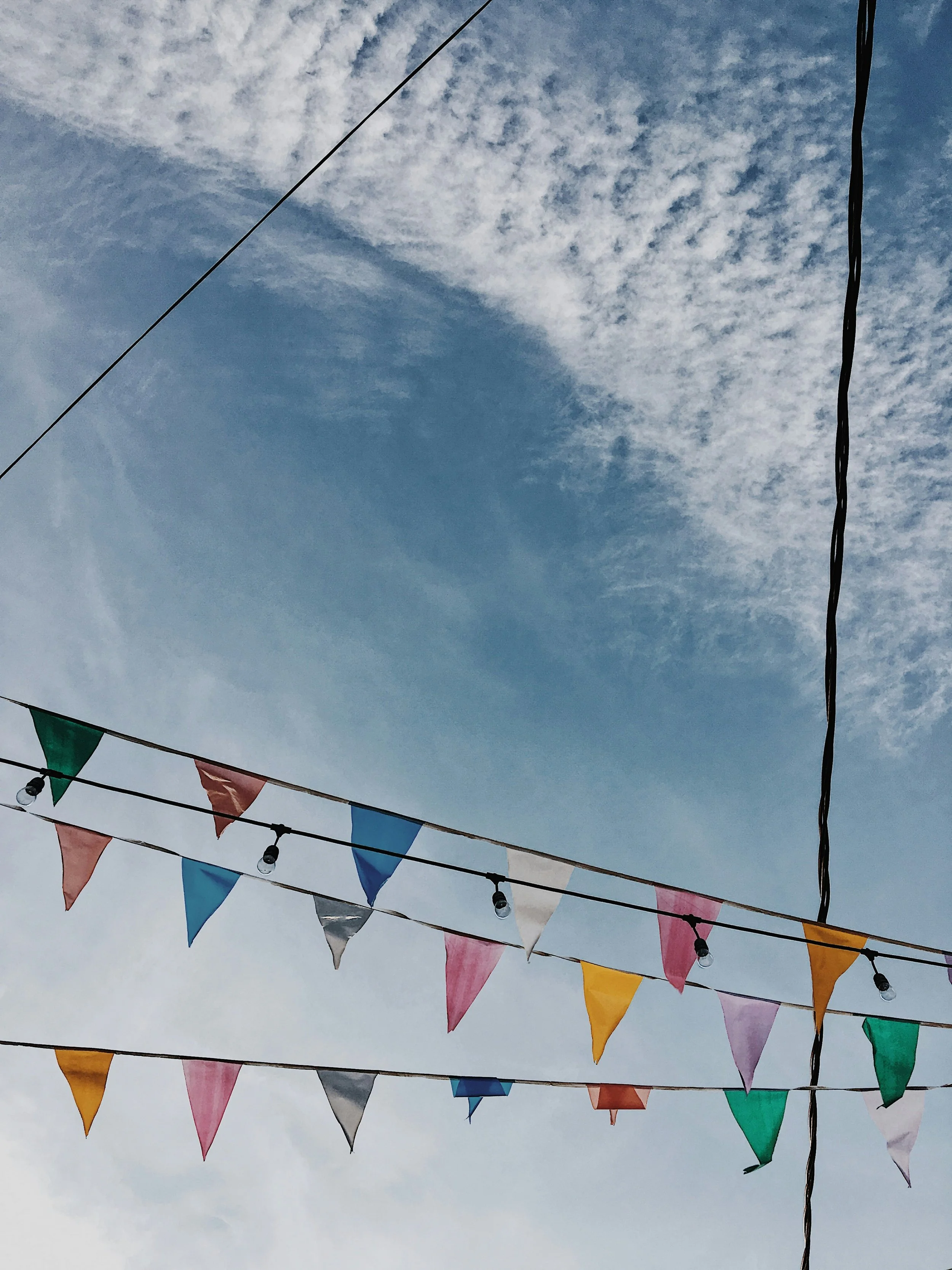 Colorful triangular flags hanging from strings against a partly cloudy sky.