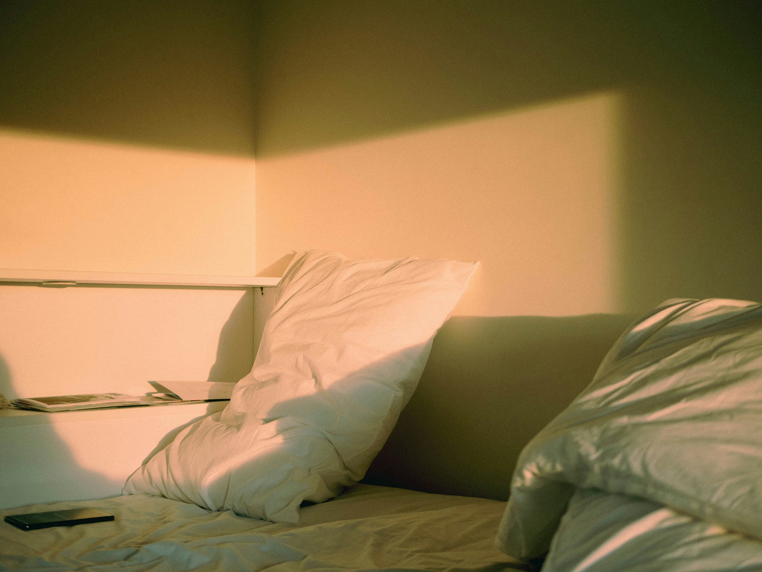 A bed with white and gray striped bedding, a pillow, a nightstand with magazines, and a smartphone at the edge, in a room with green and pink walls.
