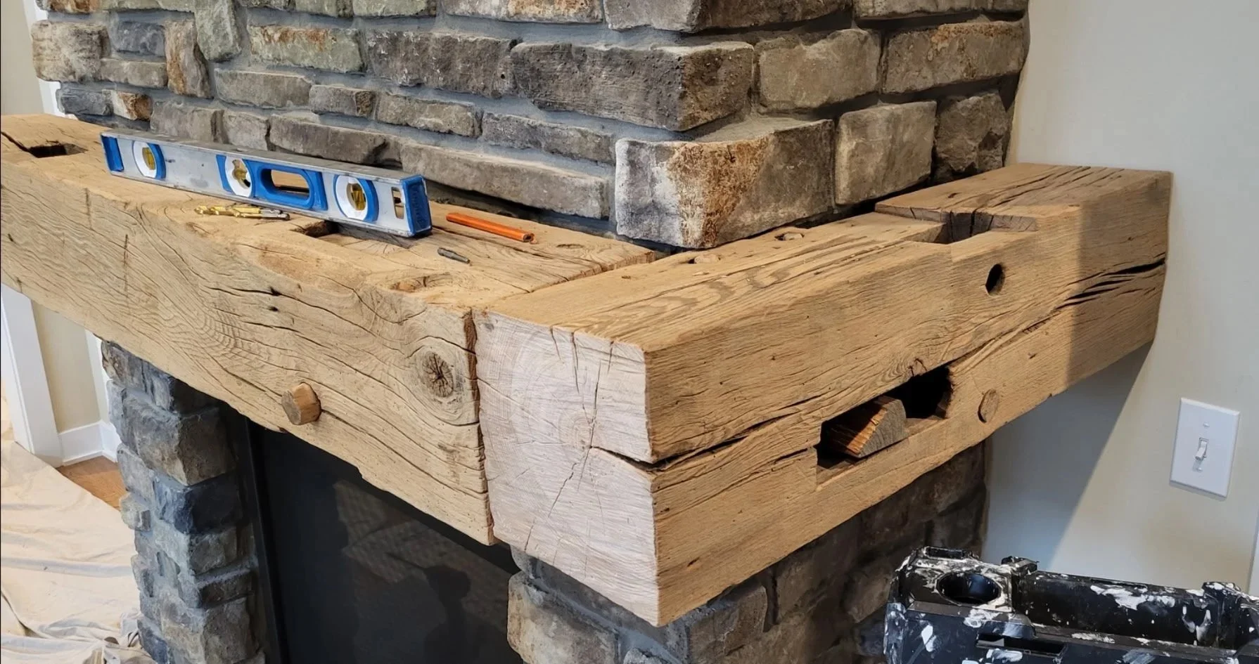 Wood beam countertop installation in progress on a brick fireplace, with a level, pencil, and screws on the surface.