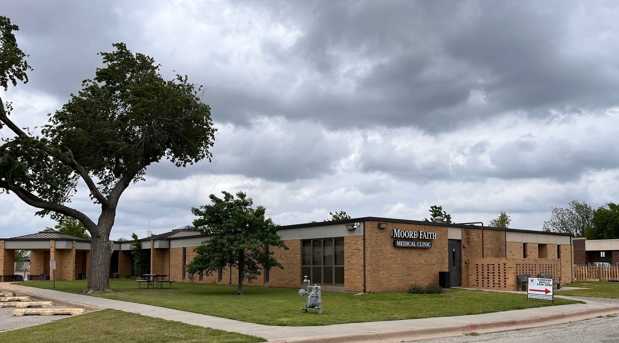 Exterior view of Moore Faith Medical Clinic building with trees, cloudy sky, and parking lot.