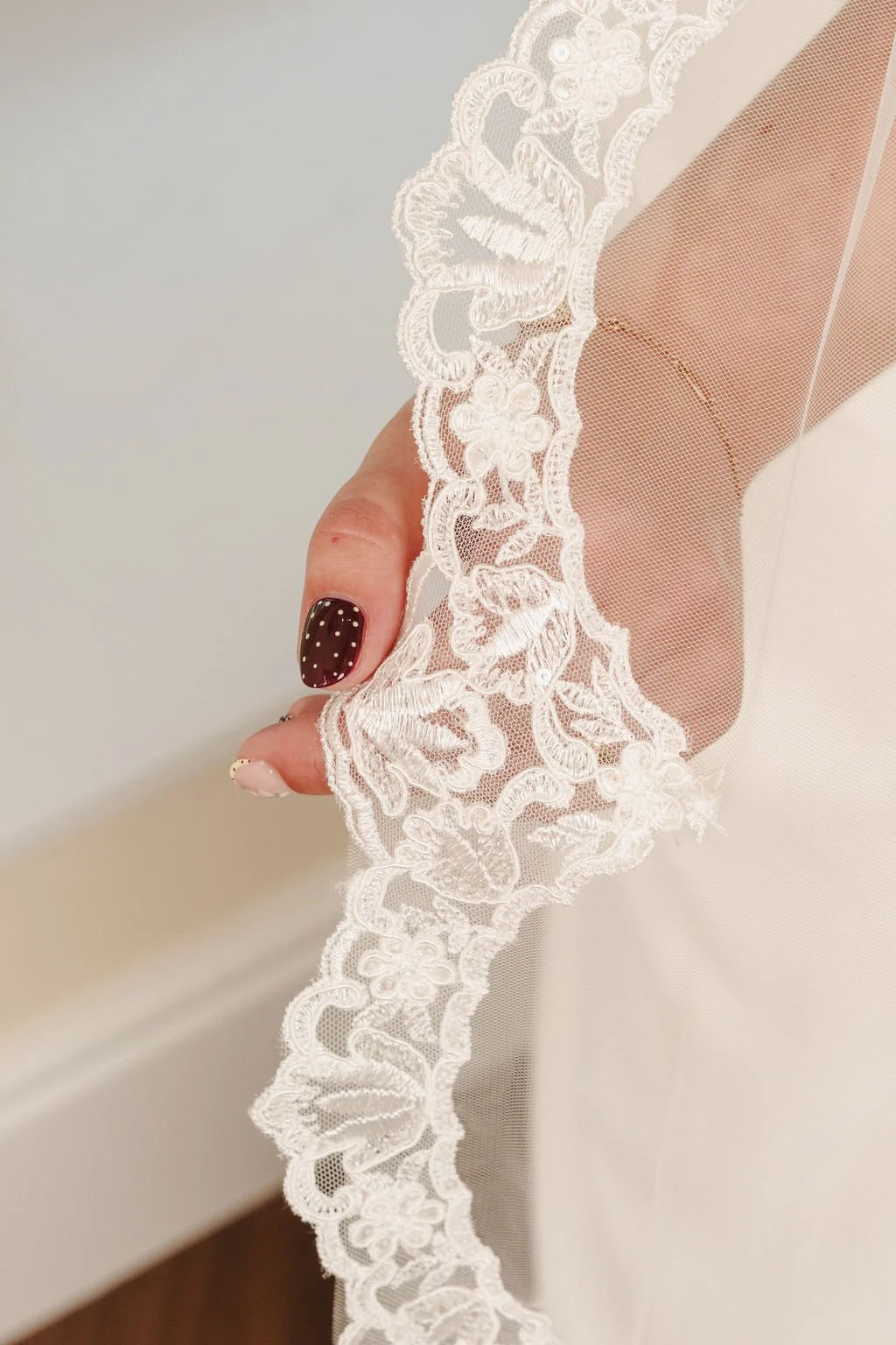 Close-up of a hand holding a piece of white lace fabric, showing intricate floral embroidery and mesh design.