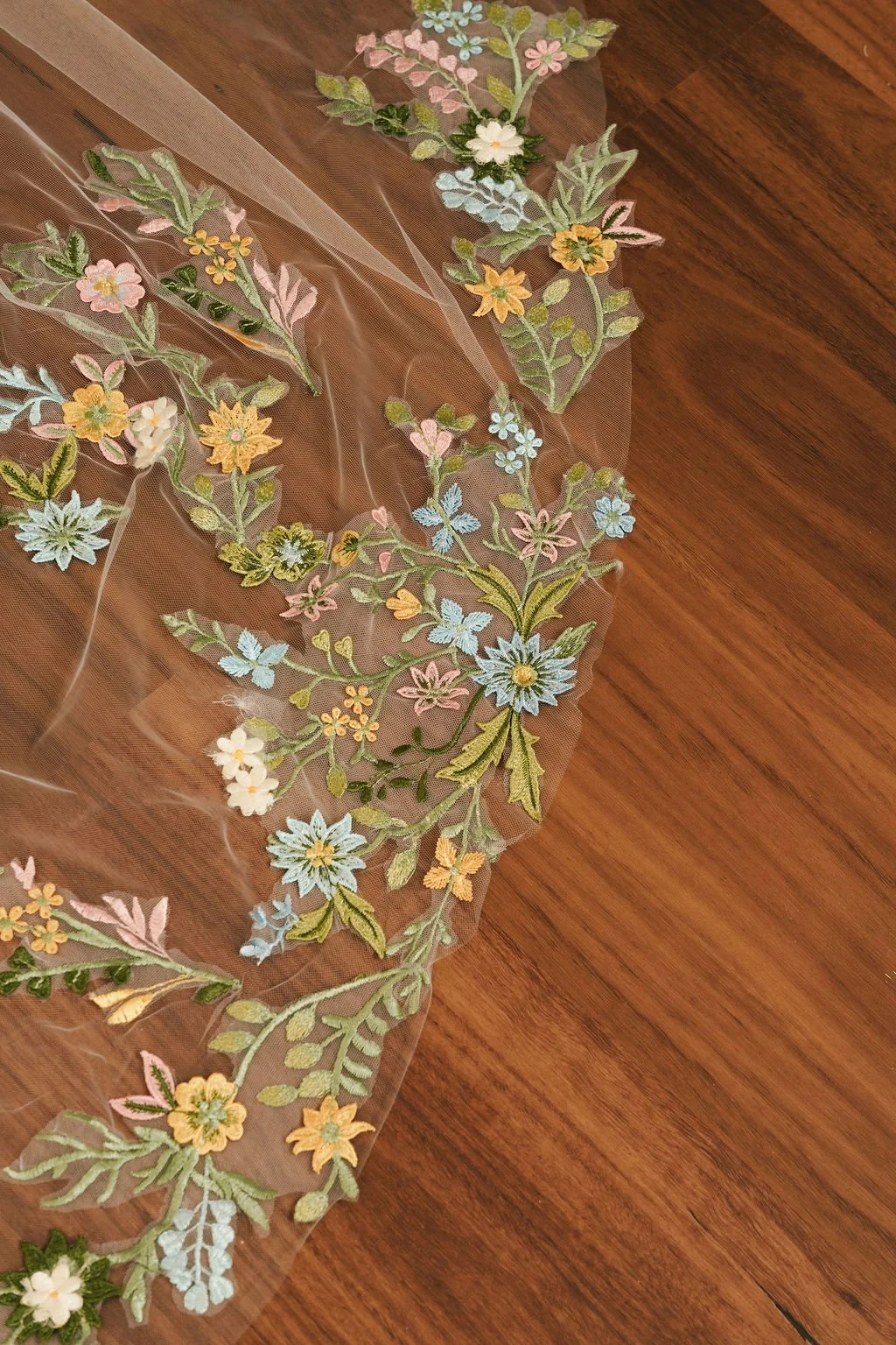 Embroidered floral design on sheer fabric laid on a wooden surface.